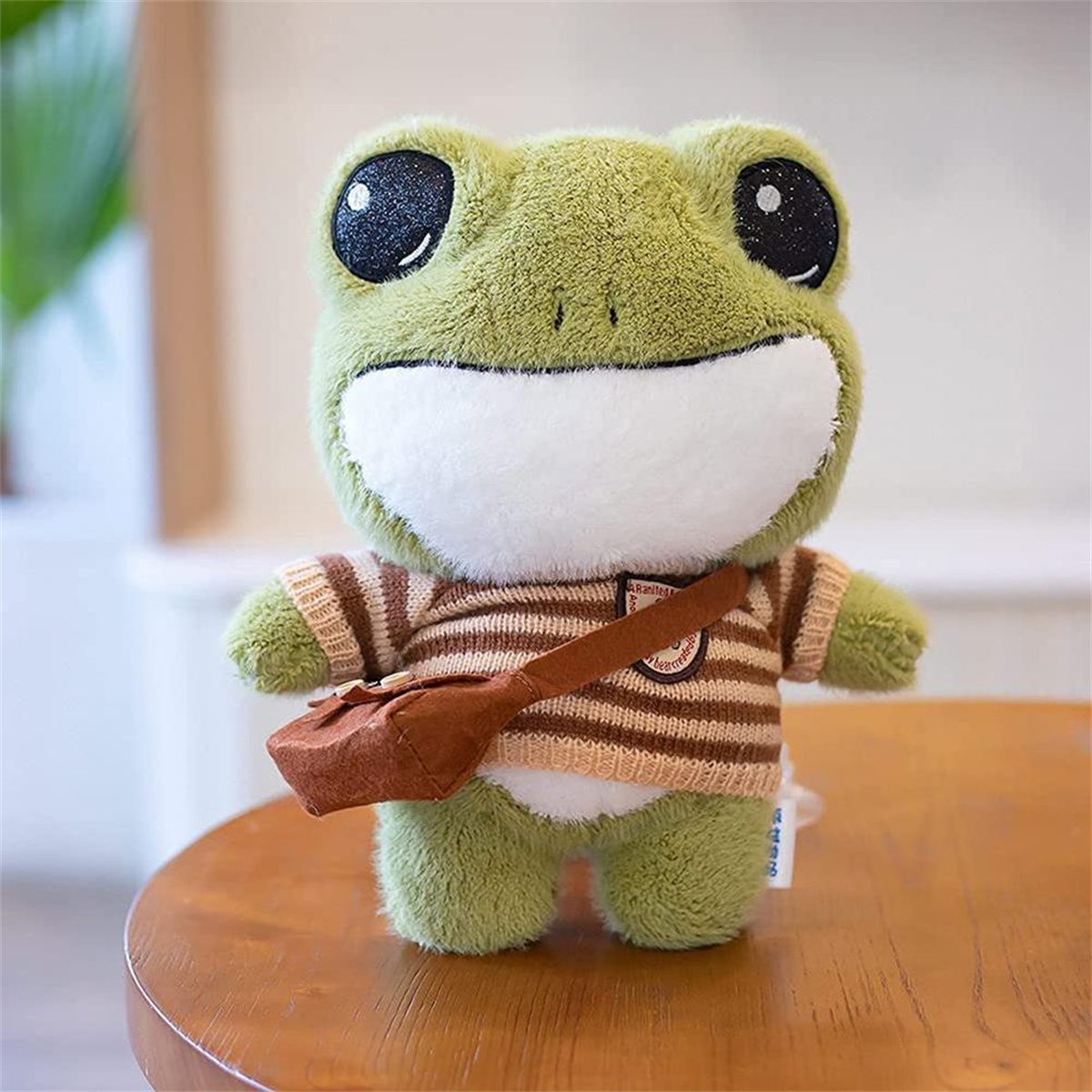Grüner Frosch-Plüschtier mit gestreiftem Hemd und brauner Tasche. Auf einem Holztisch.
