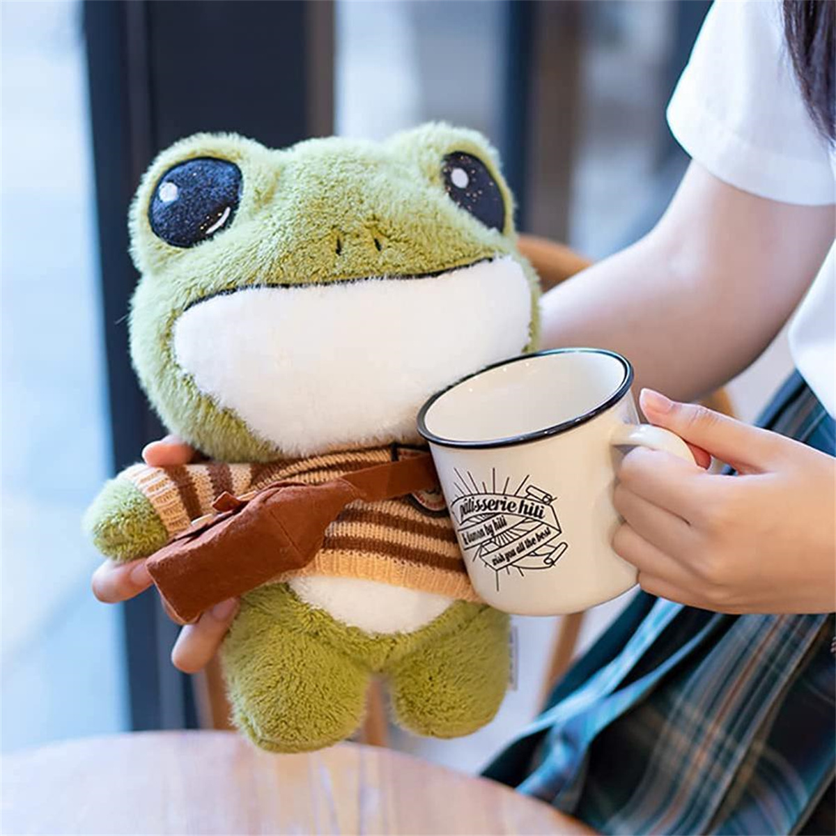 Ein grüner Frosch-Plüsch hält einen Becher. Eine Person hält den Plüsch in ihren Händen.