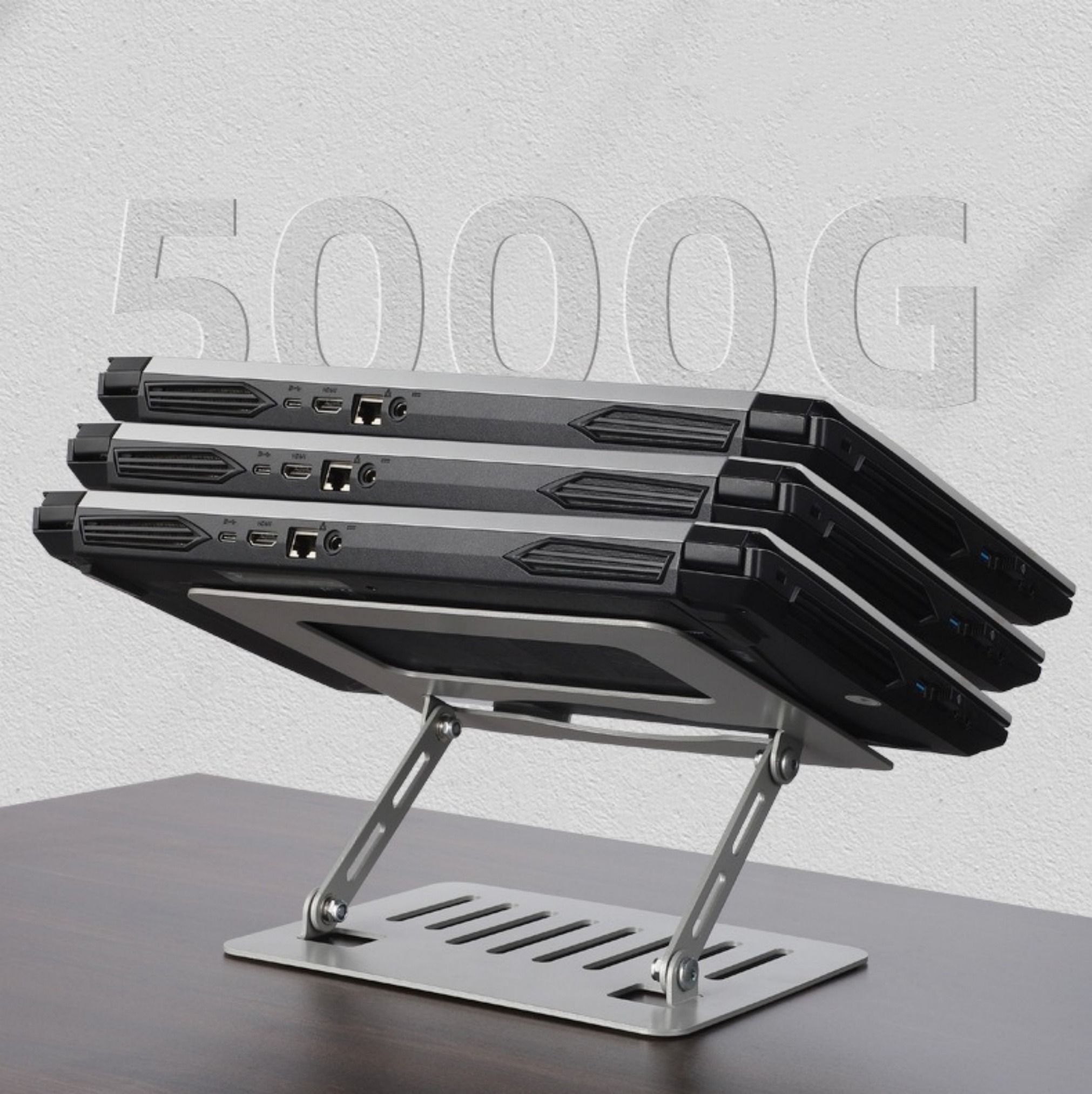 Drei Laptops auf einem silbernen Laptop-Ständer auf einem braunen Tisch, mit dem Text 5000G darüber.