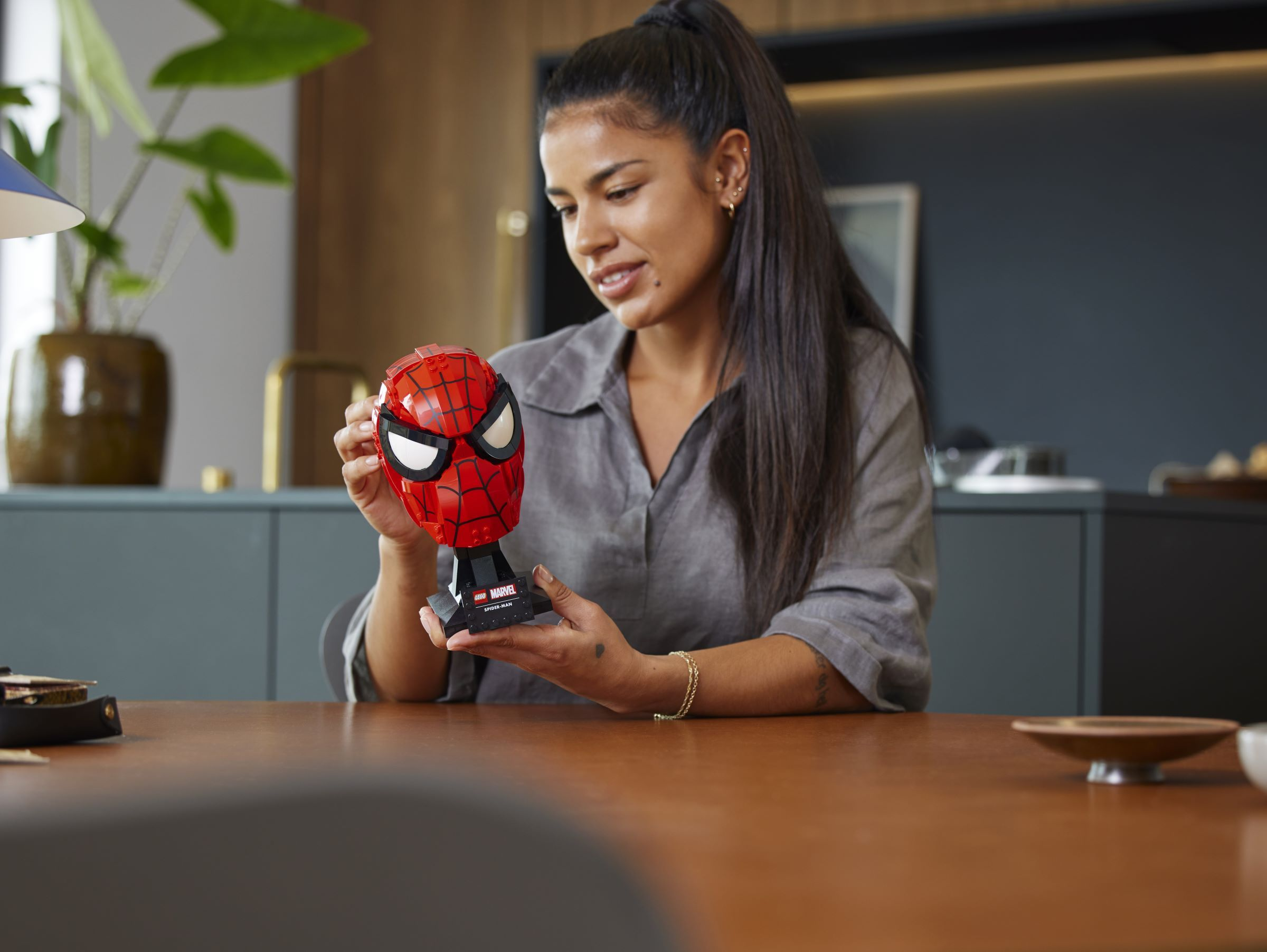 Kobieta trzyma głowę Lego Spider-Mana na stole.