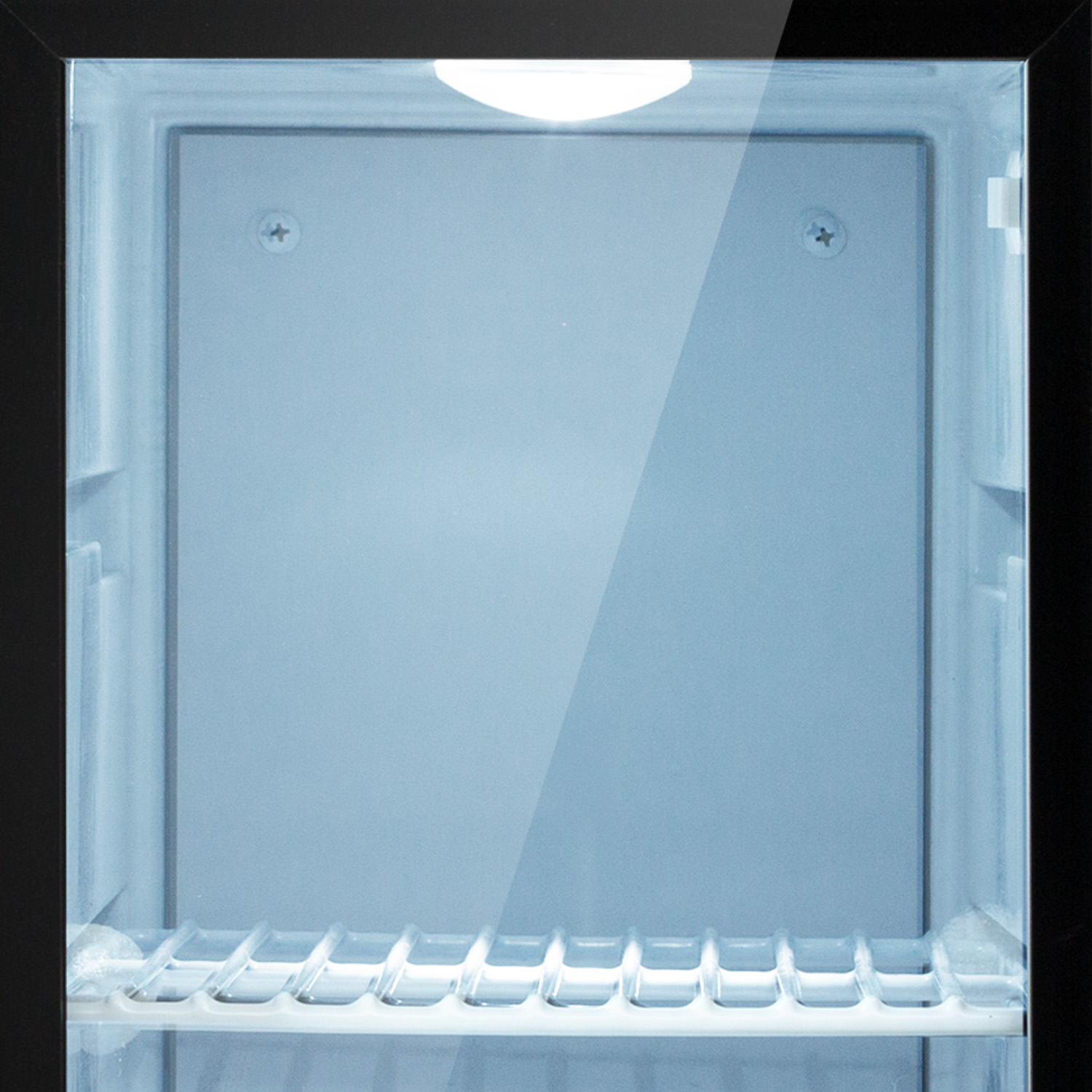 Interior vacío e iluminado de un pequeño refrigerador negro. Cuenta con una estantería y una luz brillante en la parte superior. Puerta de cristal.