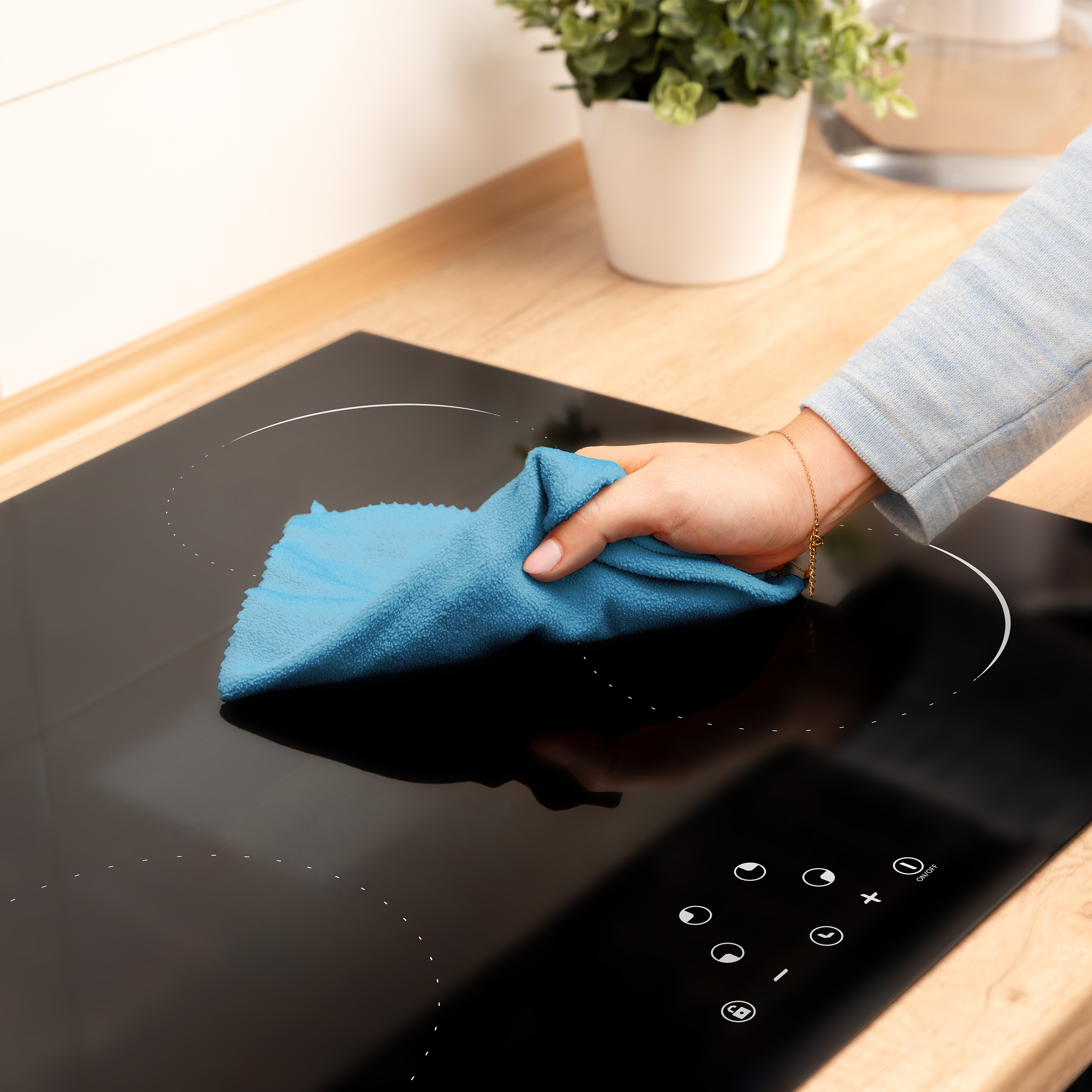 Een persoon maakt een zwart fornuis schoon met een blauwe doek. Houten aanrechtblad op de achtergrond.