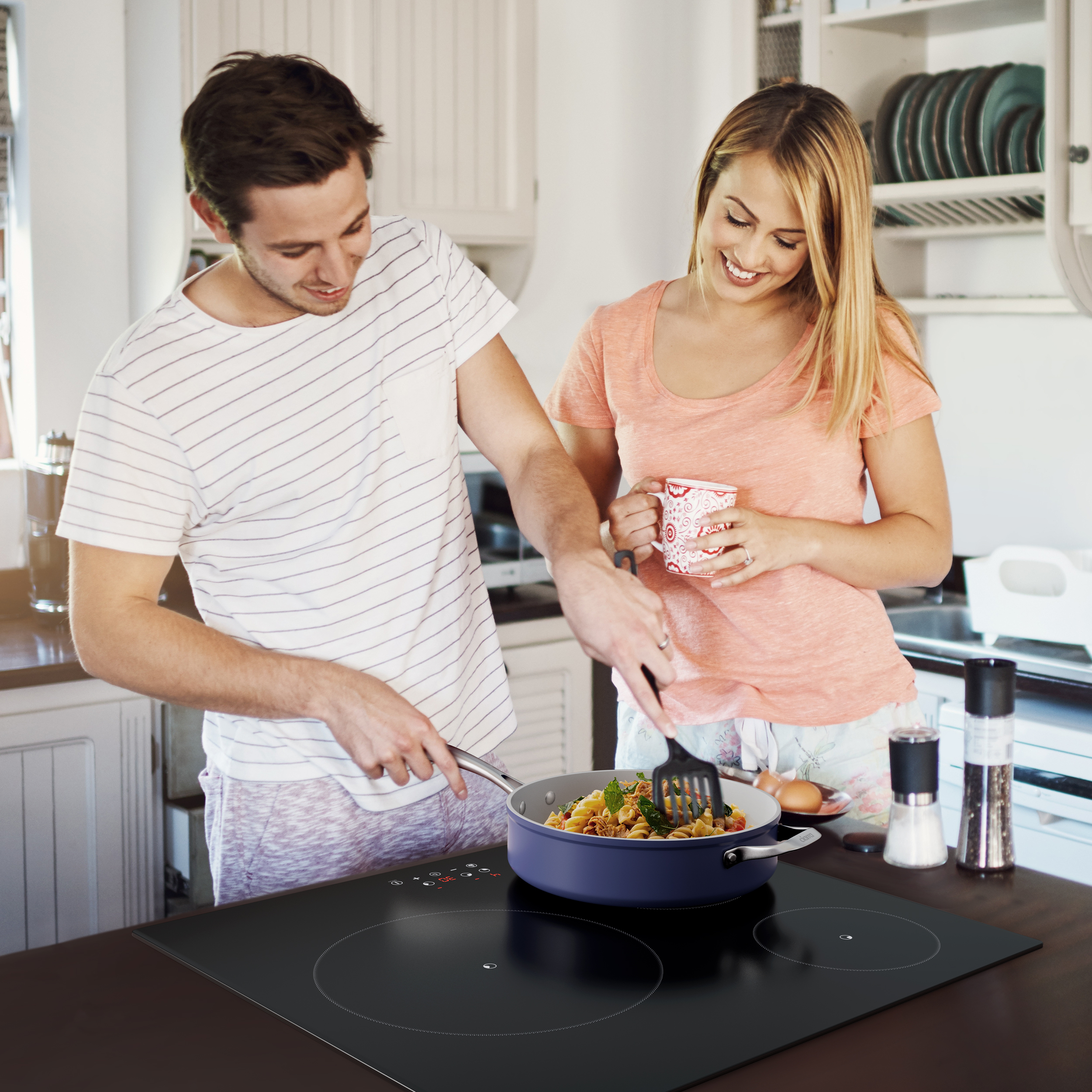 Couple cuisinant dans une cuisine. L'un remue des aliments dans une poêle sur une table de cuisson à induction.