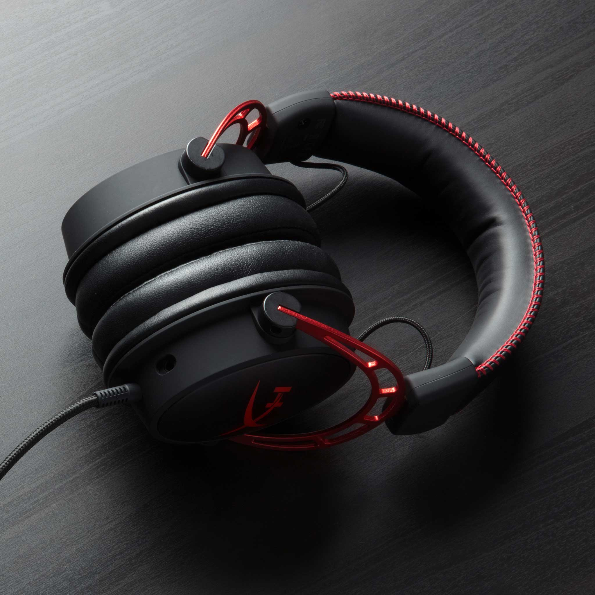 Schwarze Gaming-Kopfhörer mit roten Akzenten. Sie liegen auf einer dunklen Holzoberfläche.