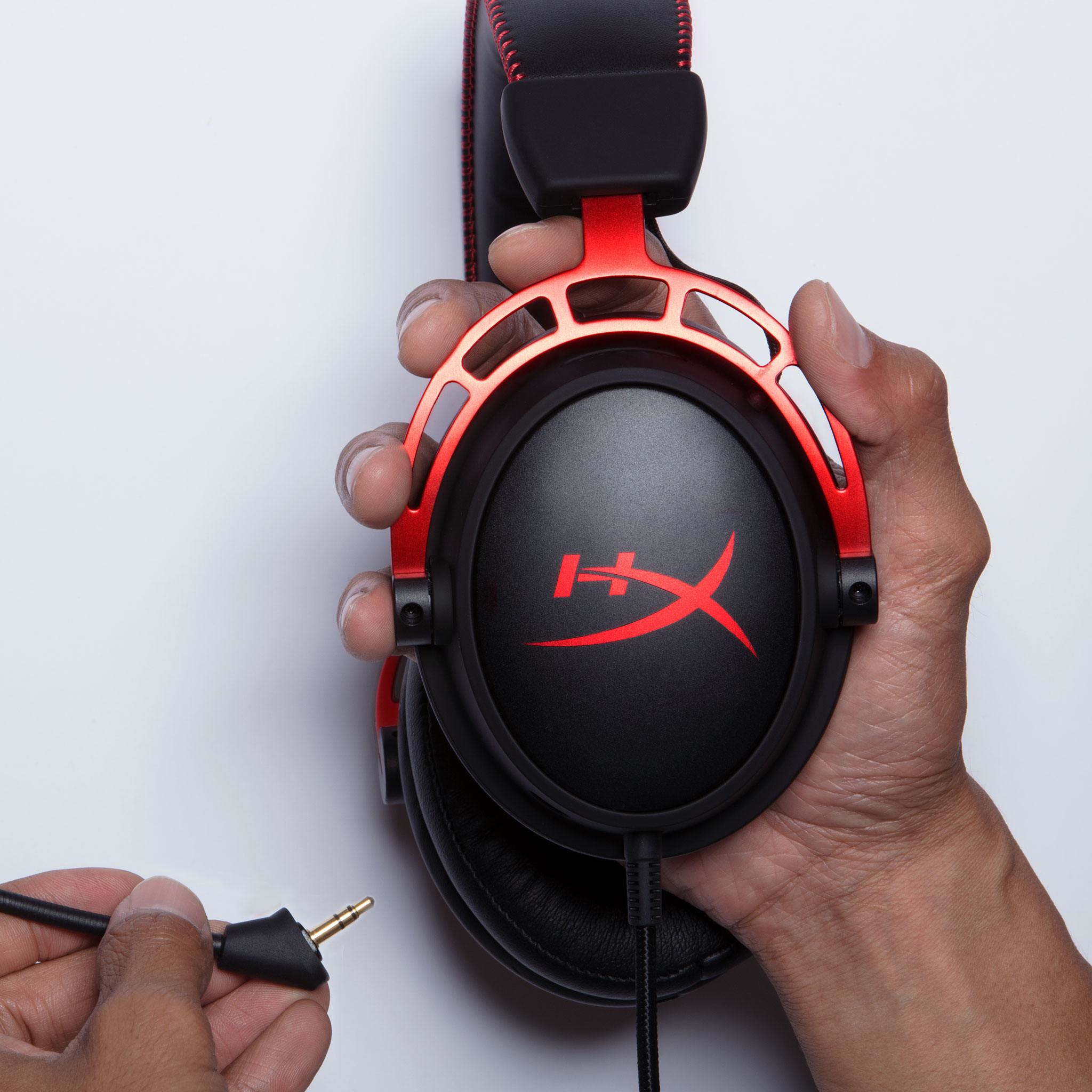 Eine Person hält ein schwarz-rotes Gaming-Headset. Das Headset hat das HyperX-Logo und ein Kabel.