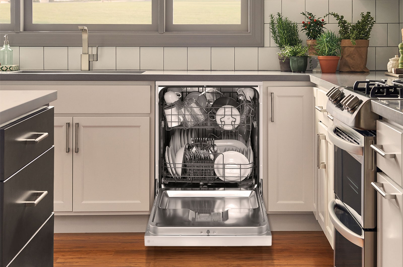 Otwarta zmywarka wypełniona czystymi naczyniami i sztućcami. Kuchnia w tle.