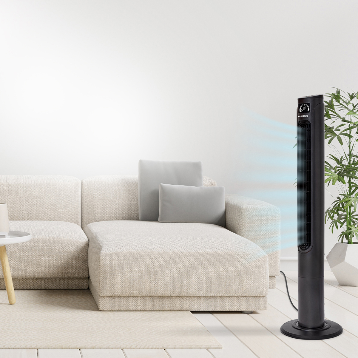 Un ventilateur tour noir près d'un canapé, soufflant de l'air vers le mur blanc.
