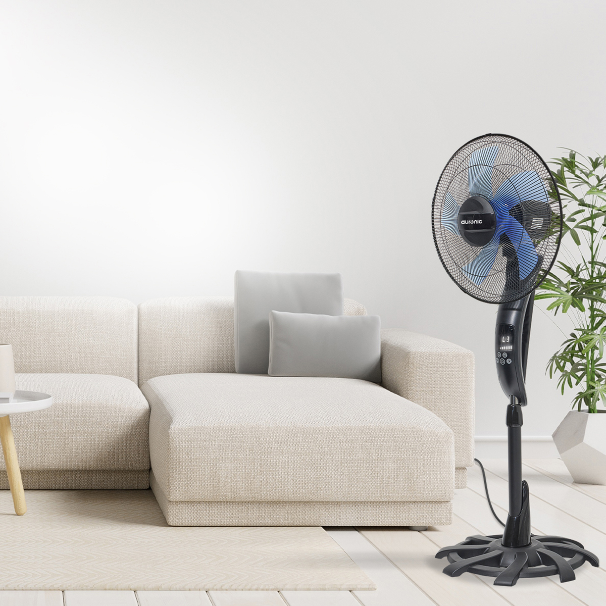 Un ventilateur sur pied noir avec des pales bleues, sur fond blanc et un canapé beige.