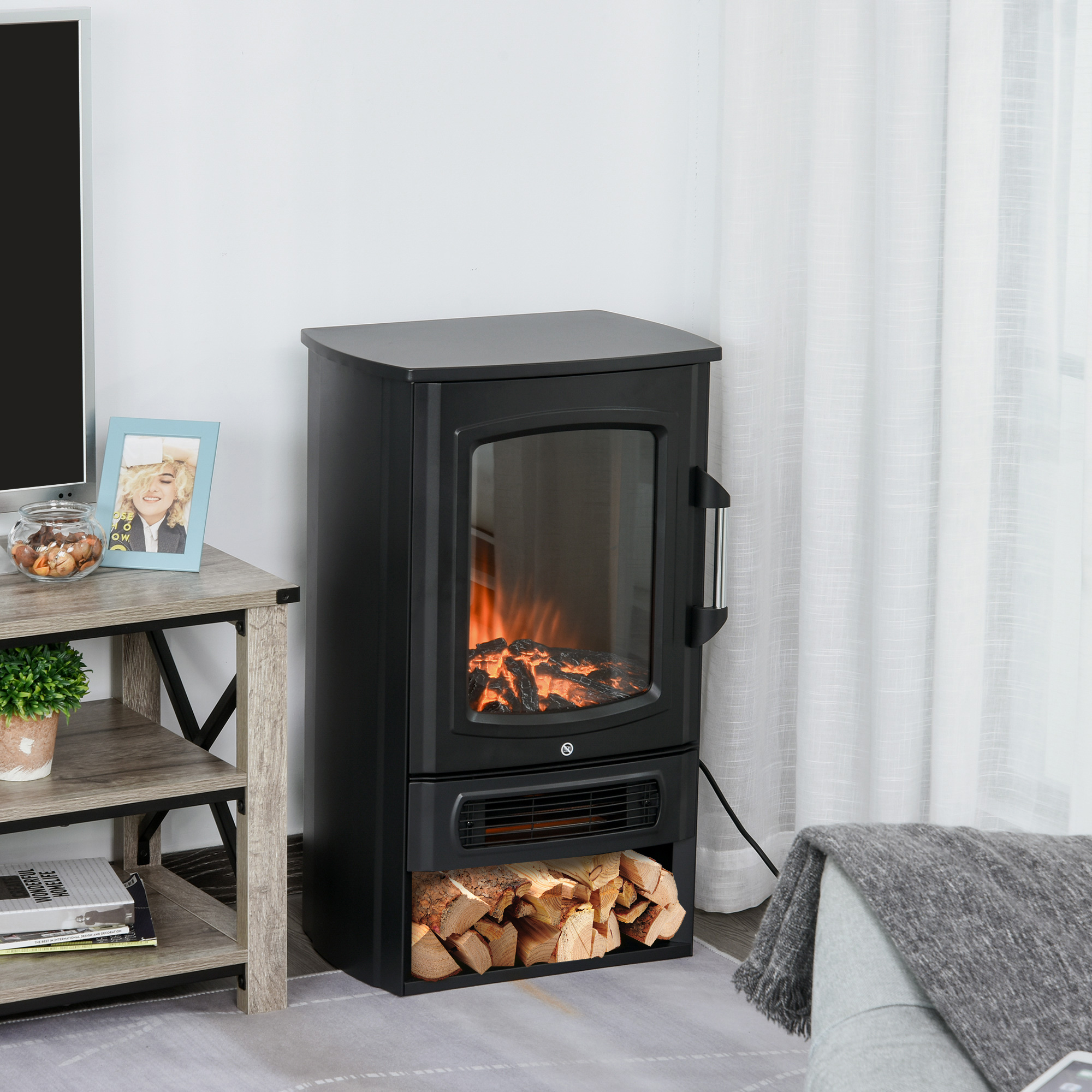 Schwarzer Elektrokamin mit Glasfront, Flammen und Holzscheiten, umgeben von einer Raumumgebung.