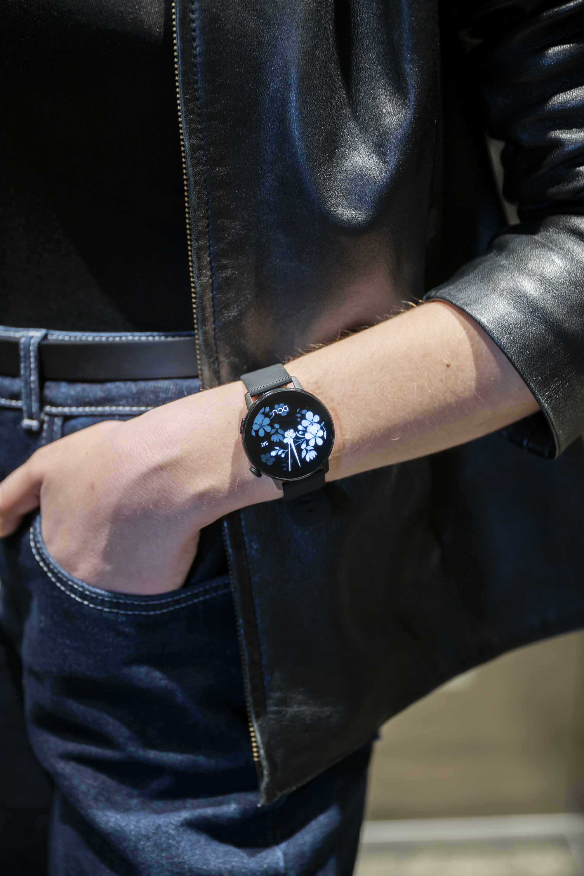 Osoba w czarnej skórzanej kurtce i niebieskich dżinsach, ze smartwatchem na nadgarstku.