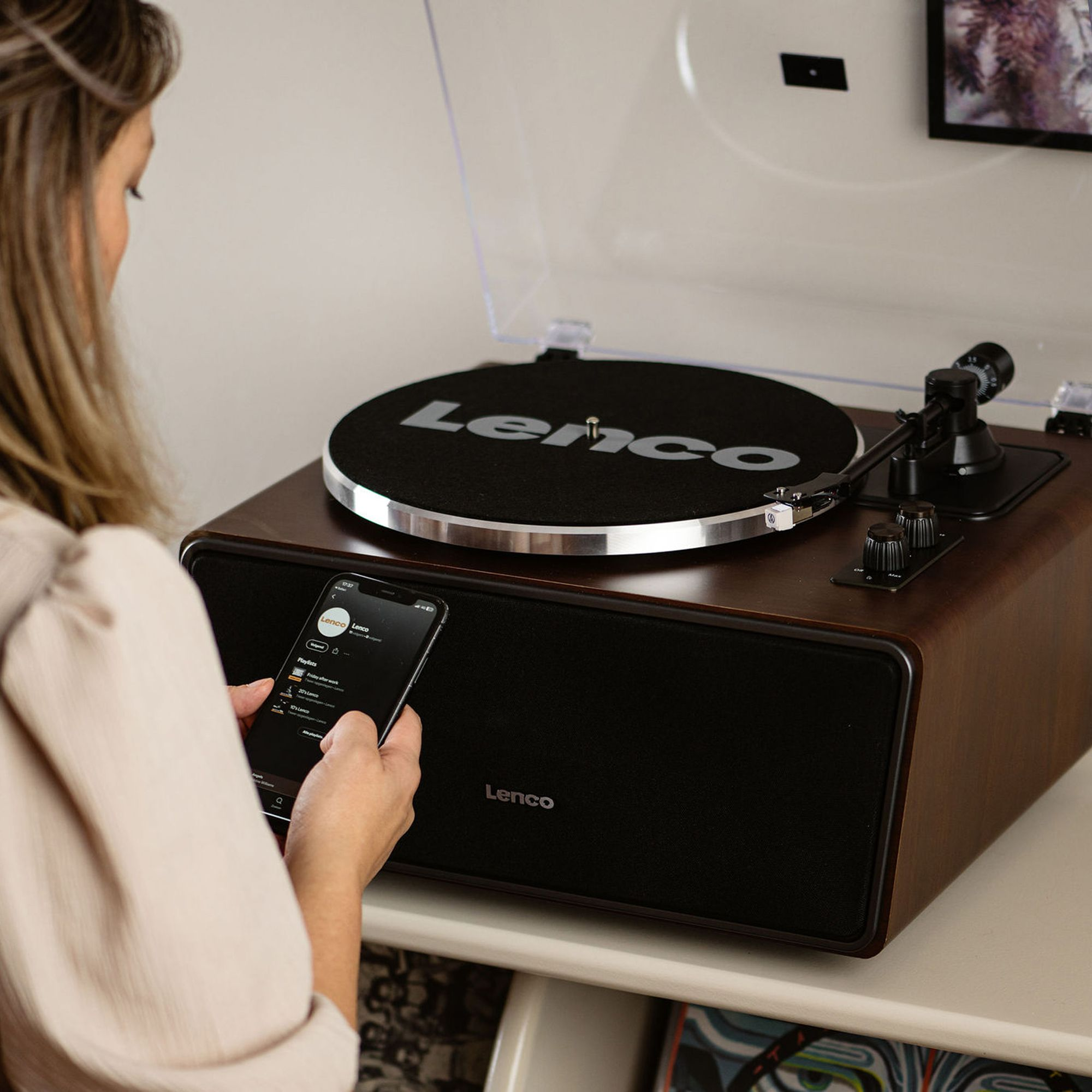 A woman is using a smartphone and listening to music on a record player with a wood finish.