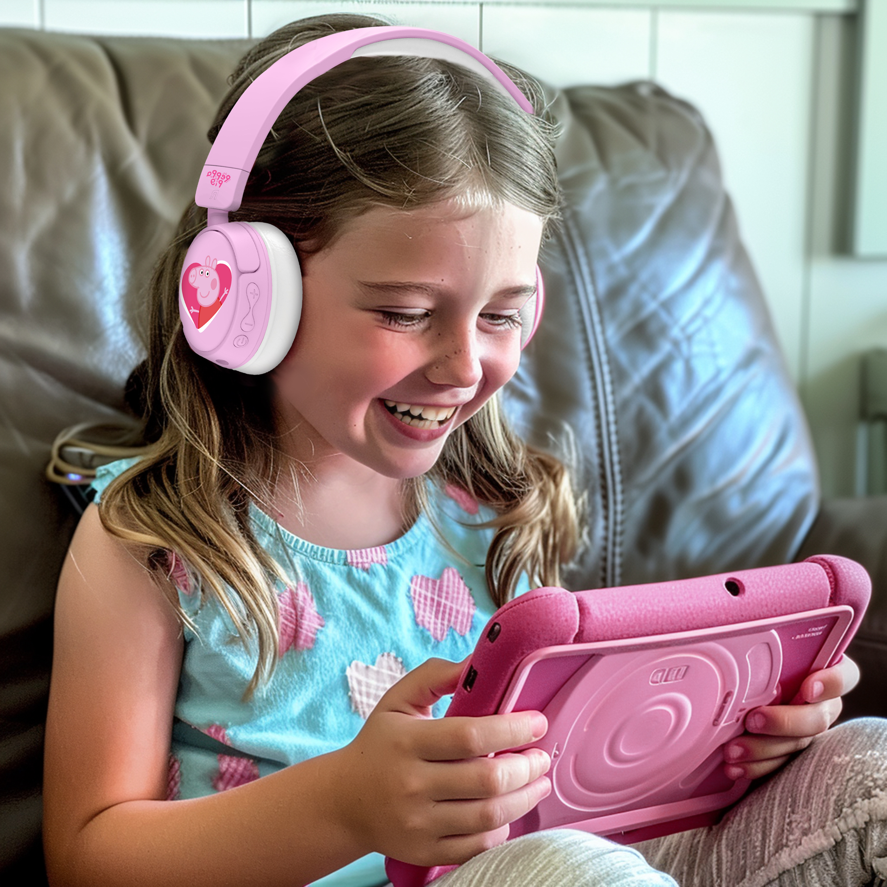 Una ragazza con le cuffie rosa di Peppa Pig sorride mentre usa un tablet. È in casa.