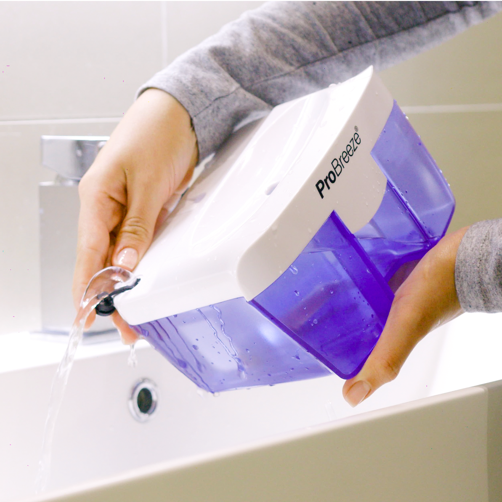 Una persona versa acqua da un contenitore bianco e viola in un lavandino bianco.