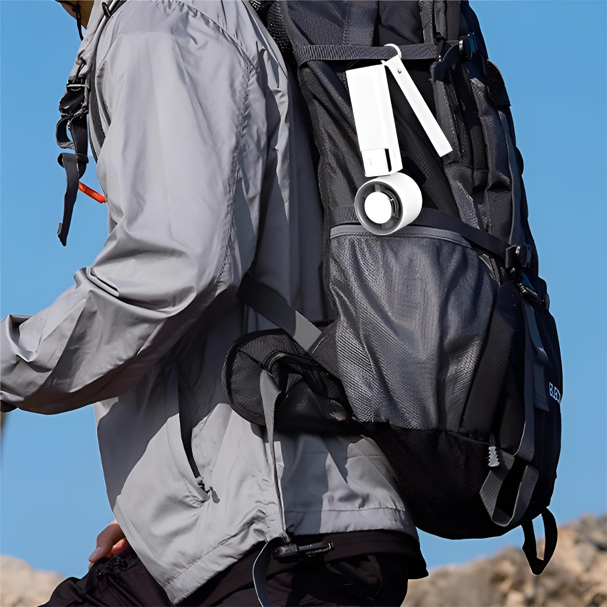 Eine Person in grauer Jacke beim Wandern mit schwarzem Rucksack. Ein Ventilator ist am Rucksack befestigt.