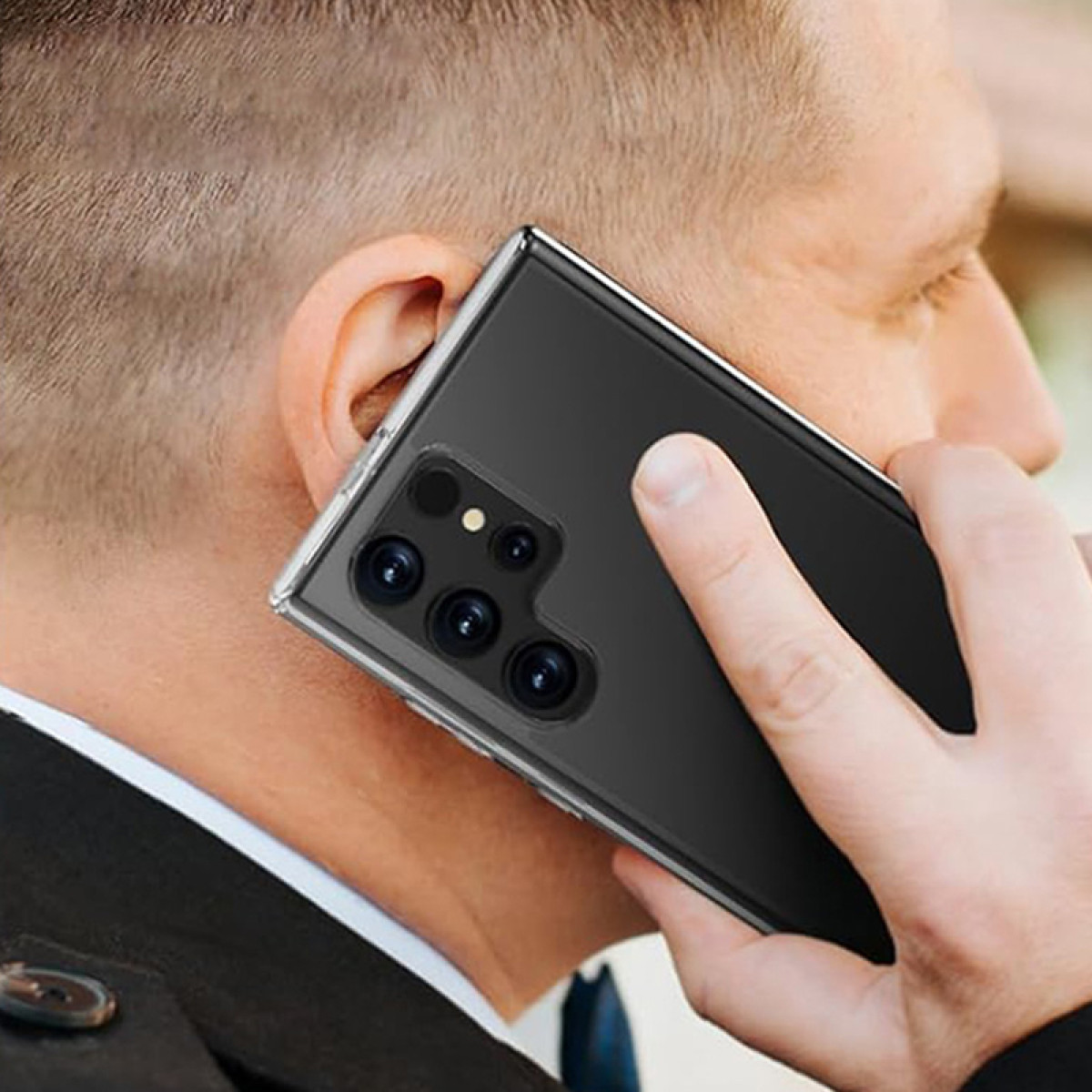Un uomo al telefono, mostra un telefono con più fotocamere. Il telefono è nero, in una custodia trasparente.