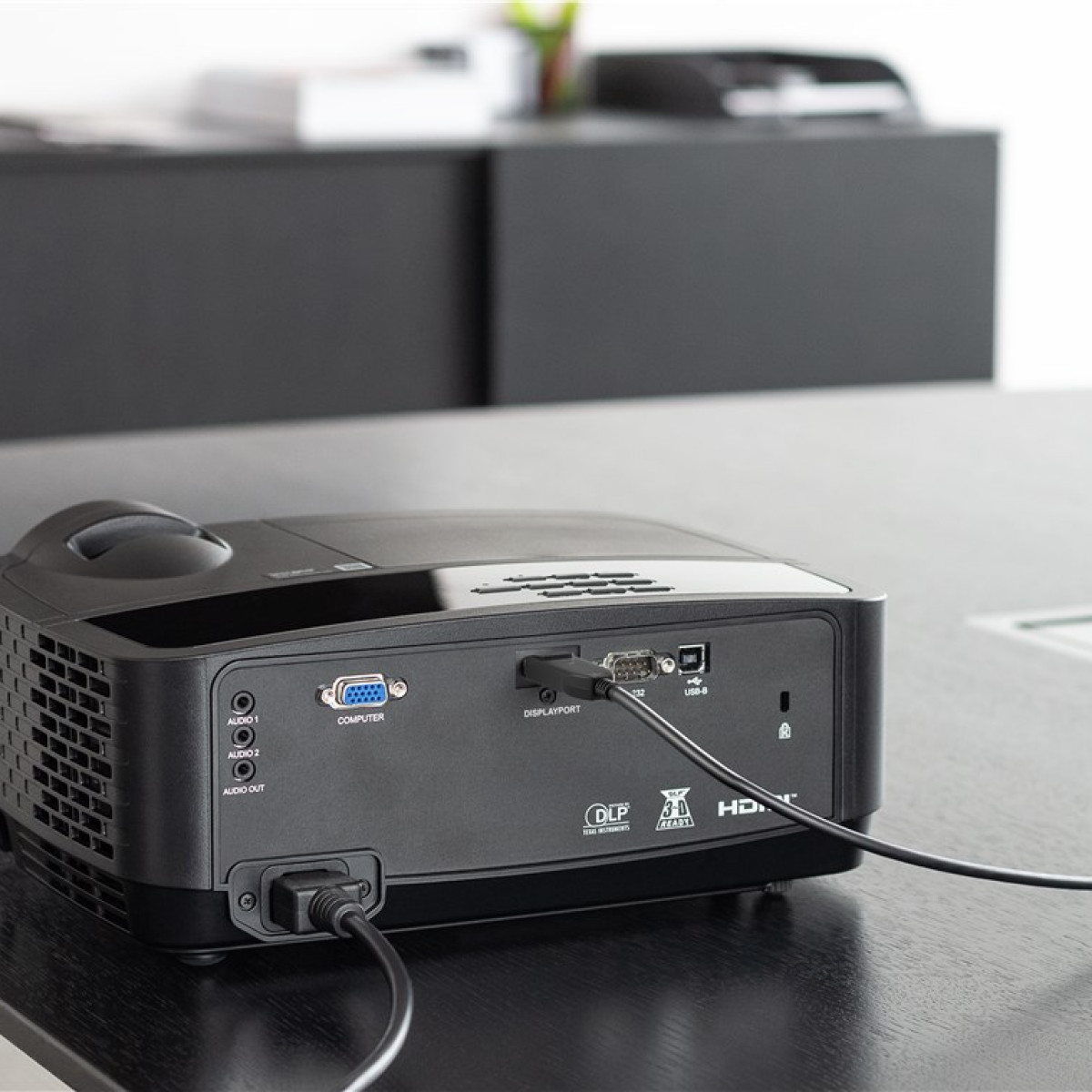 Zwarte projector met aangesloten kabels, op een zwarte tafel.