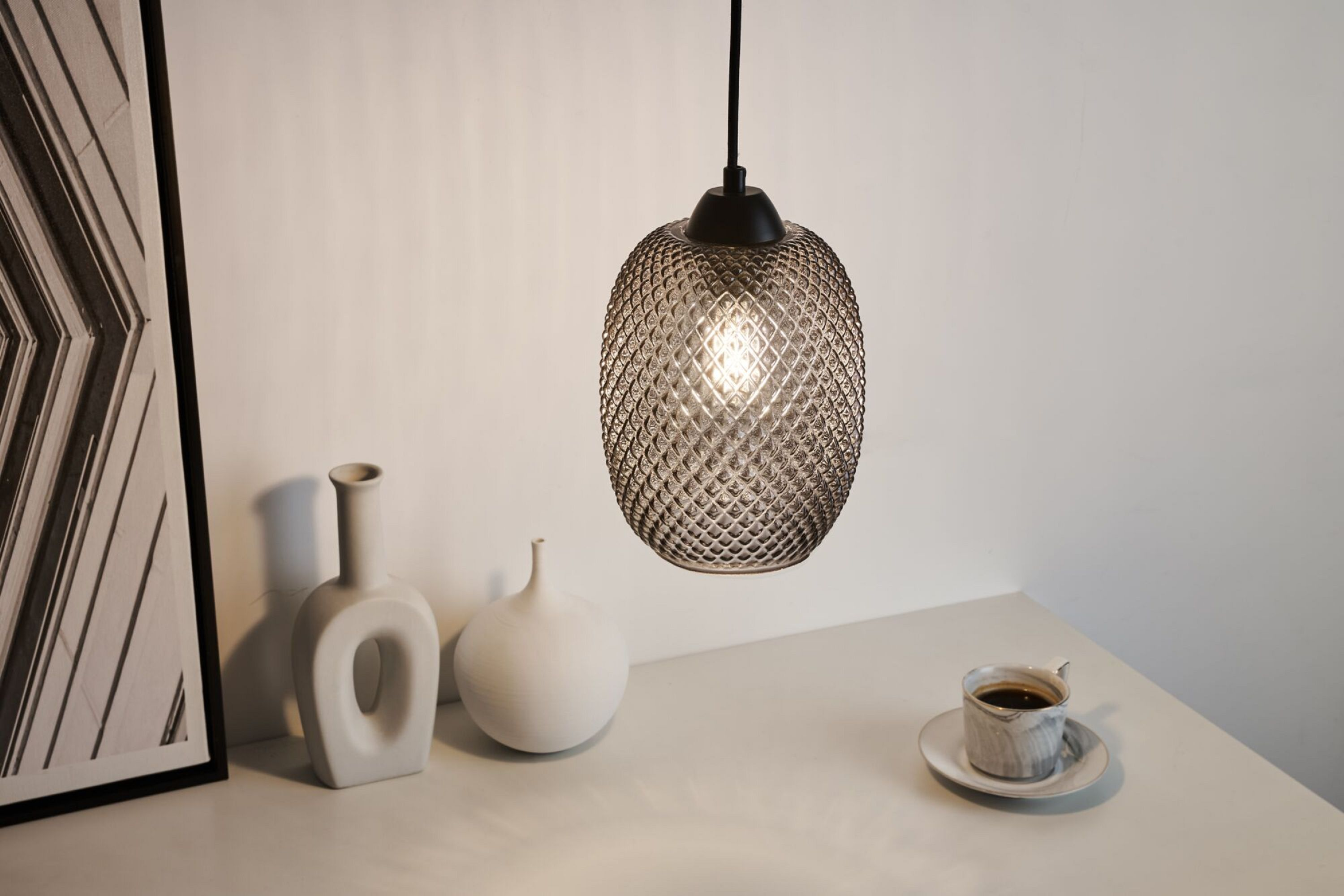 Hängende Glas-Pendelleuchte mit strukturierter Oberfläche, beleuchtet einen weißen Tisch mit Deko.