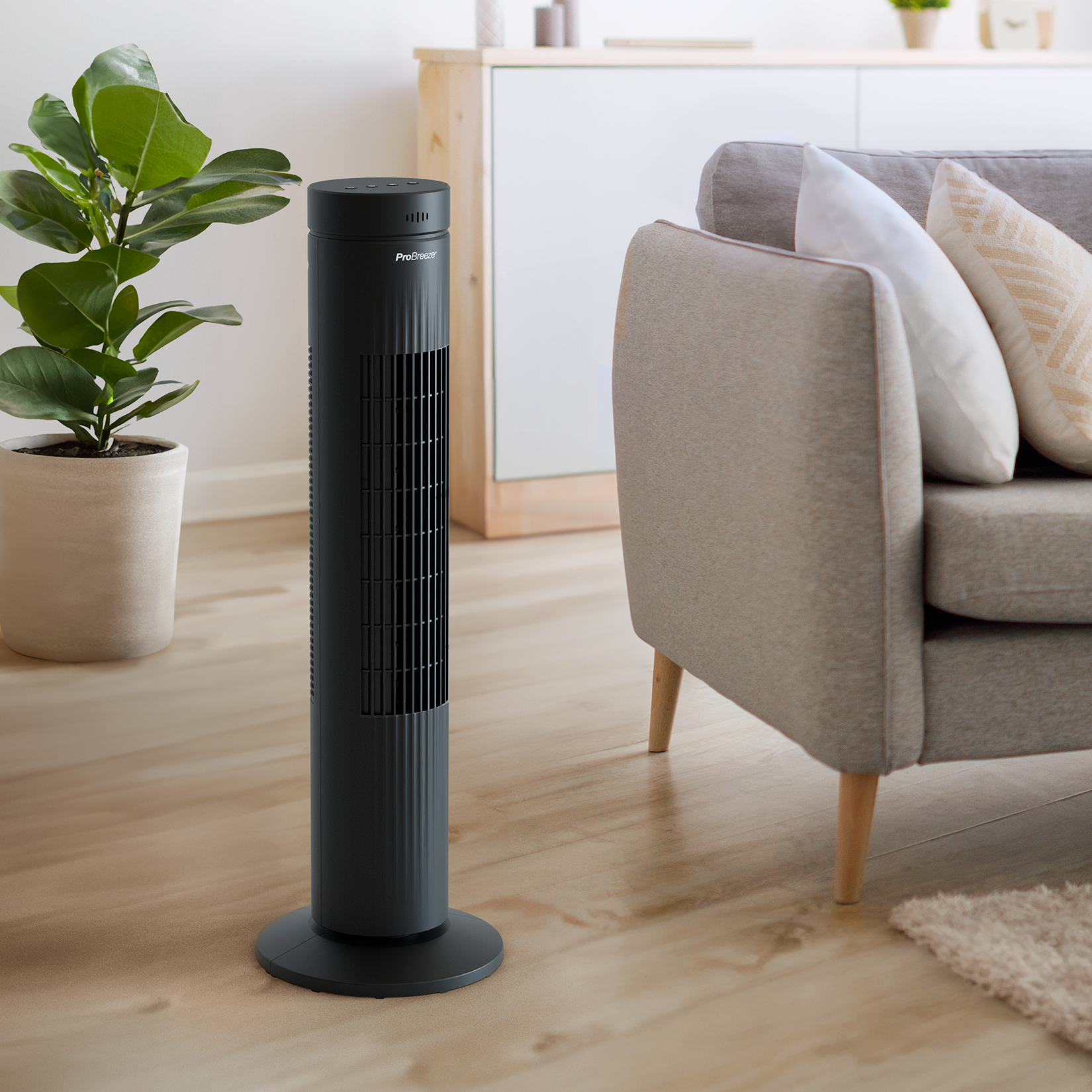 Schwarzer Turmventilator auf Holzboden, neben Sofa und Pflanze.