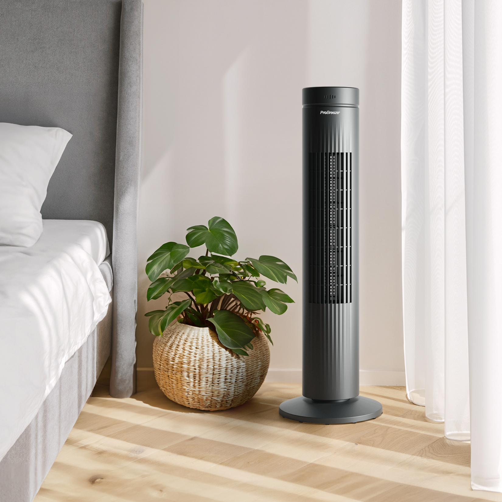 Ein grauer Turmventilator neben einer Topfpflanze und einem Bett.