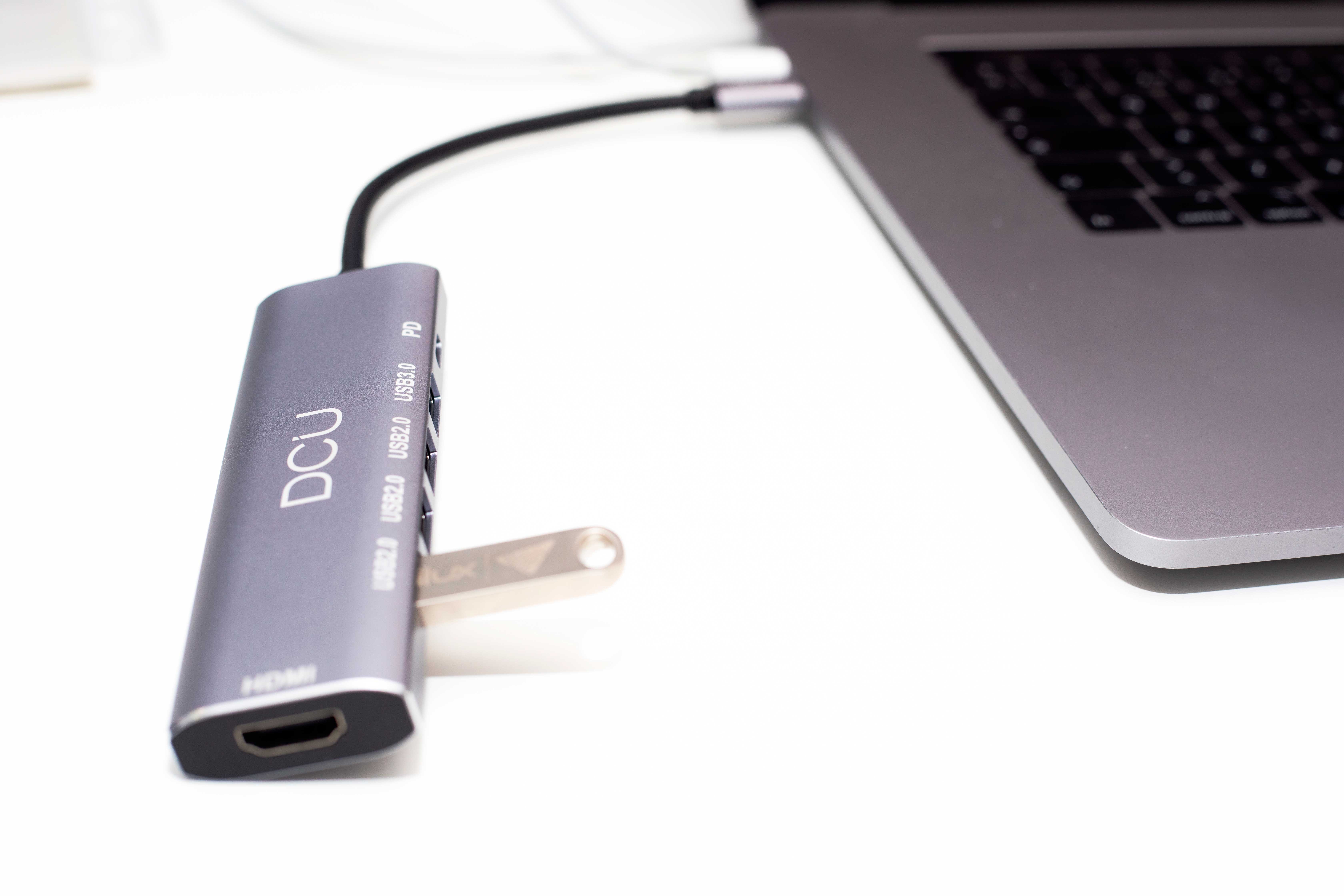 Un concentrador USB plateado conectado a una laptop. Una unidad USB está enchufada al concentrador.