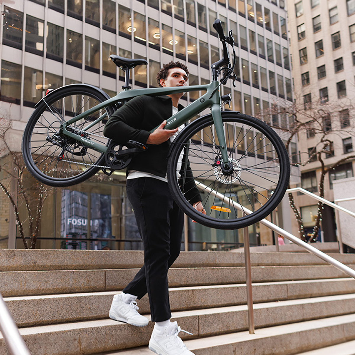 Mężczyzna niesie zielony rower na ramieniu, idzie po schodach w środowisku miejskim.