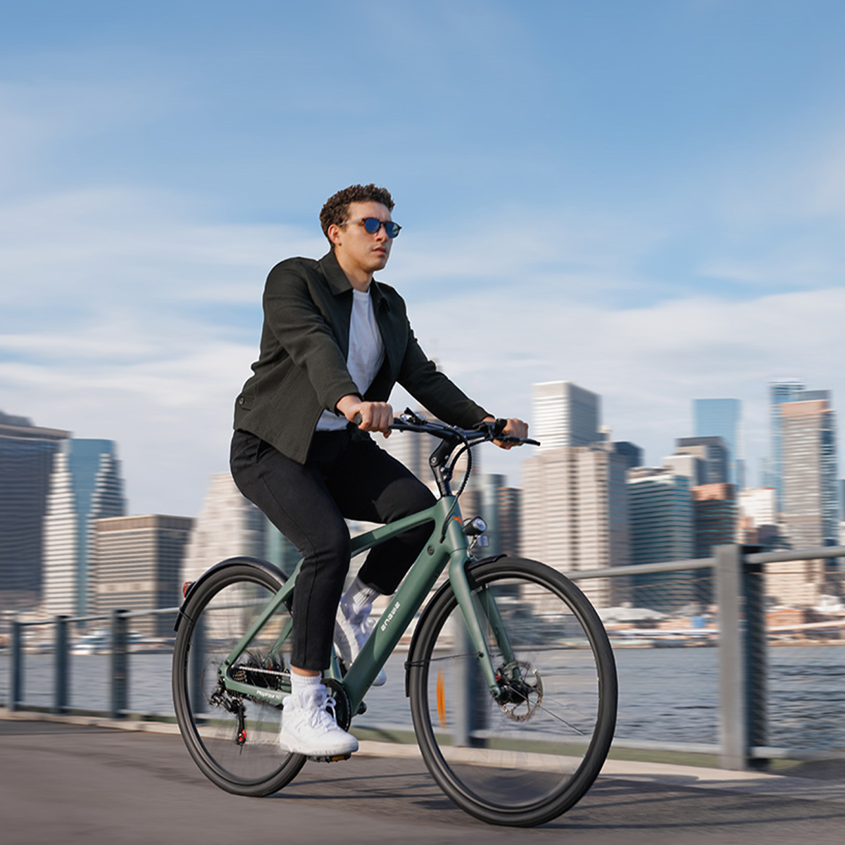 Mężczyzna jadący na zielonym rowerze ścieżką obok rzeki. Budynki w tle.