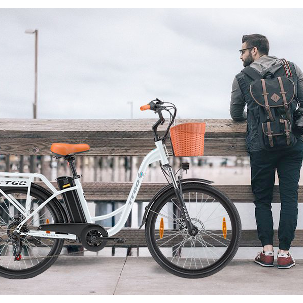 Mężczyzna opiera się o drewnianą balustradę obok biało-czarnego roweru z koszykiem.