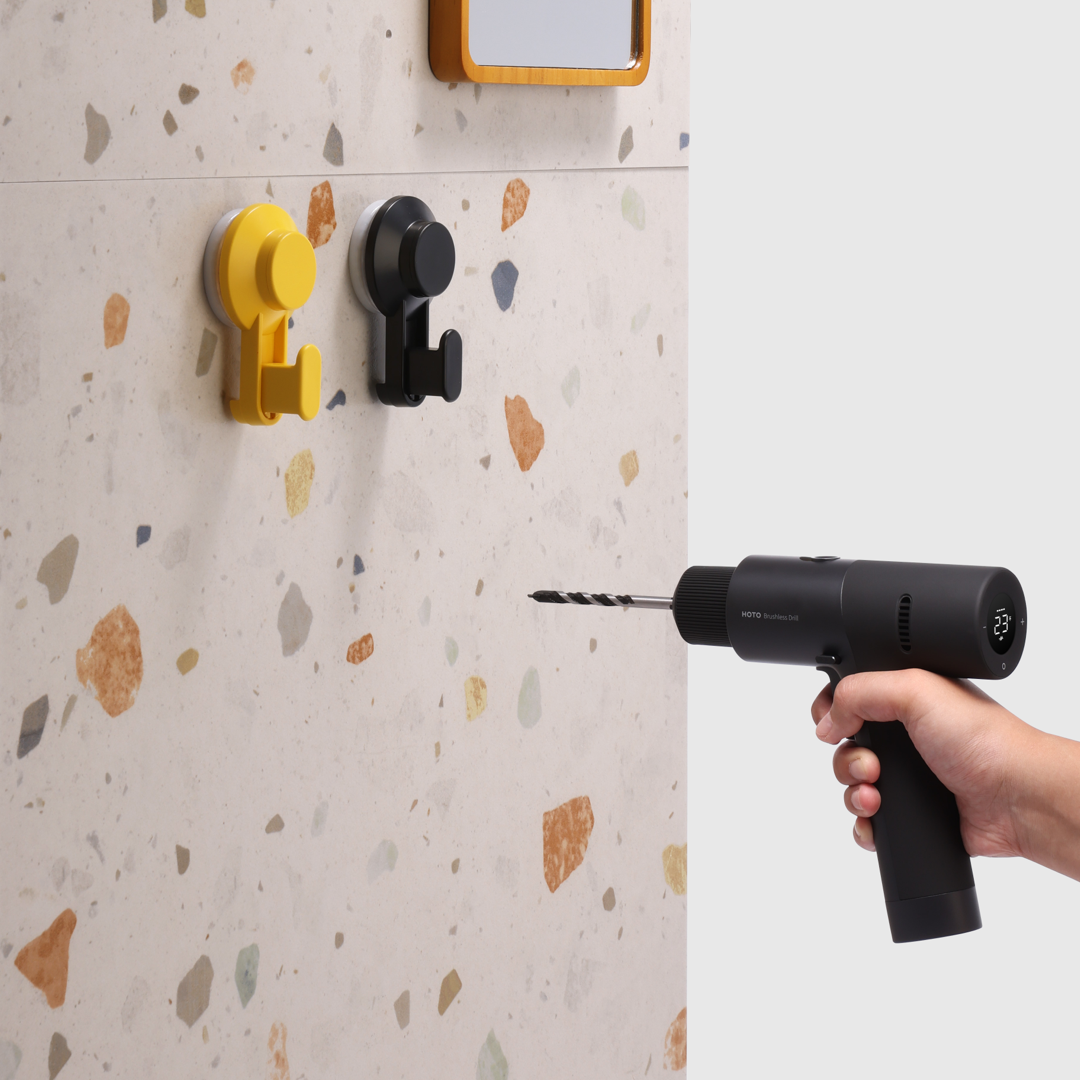Eine Person bohrt in eine Wand. Gelbe und schwarze Haken sind an einer gemusterten Wand montiert.