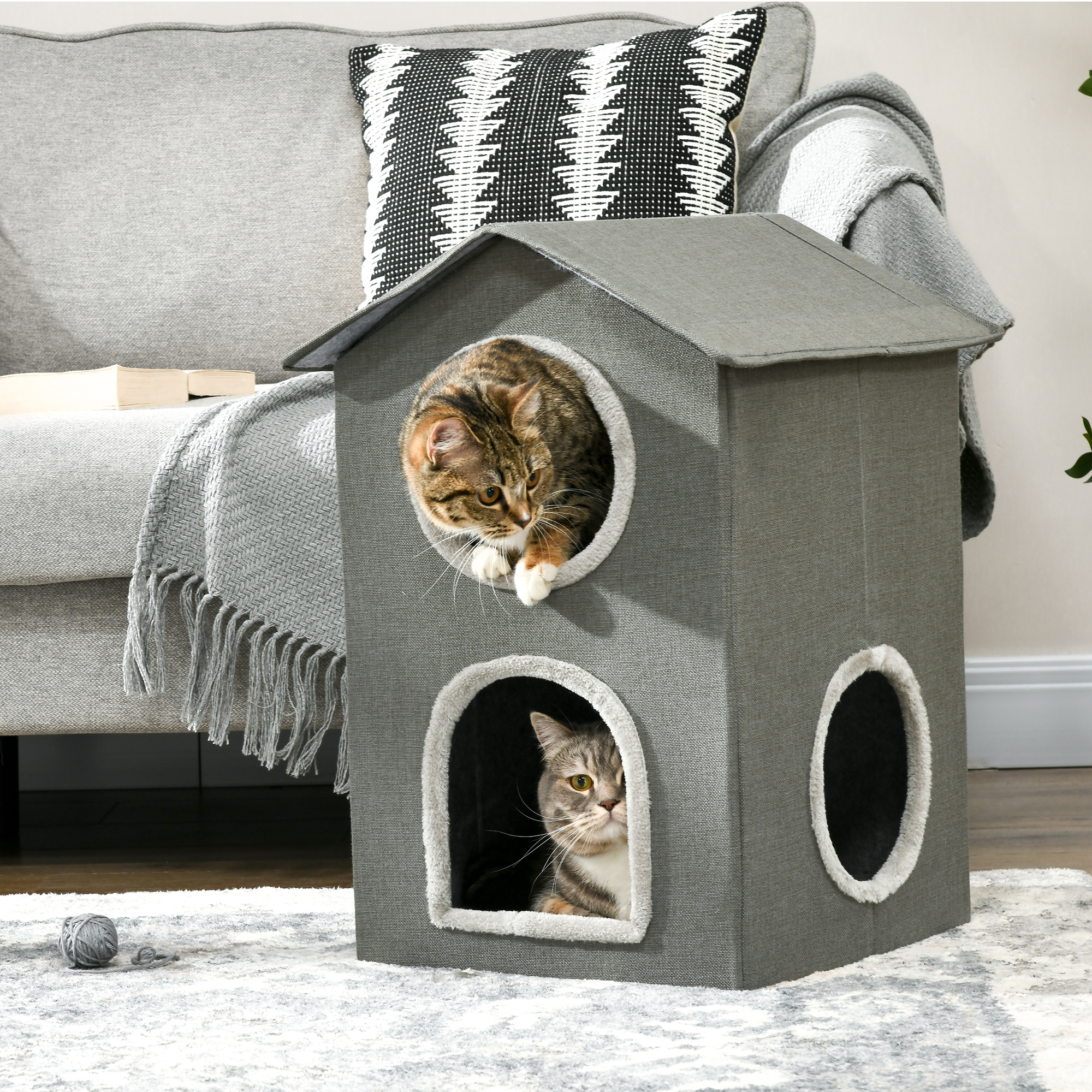Una casa gris para gatos con dos aberturas redondas y un gato en cada una. La casa está sobre una alfombra estampada.