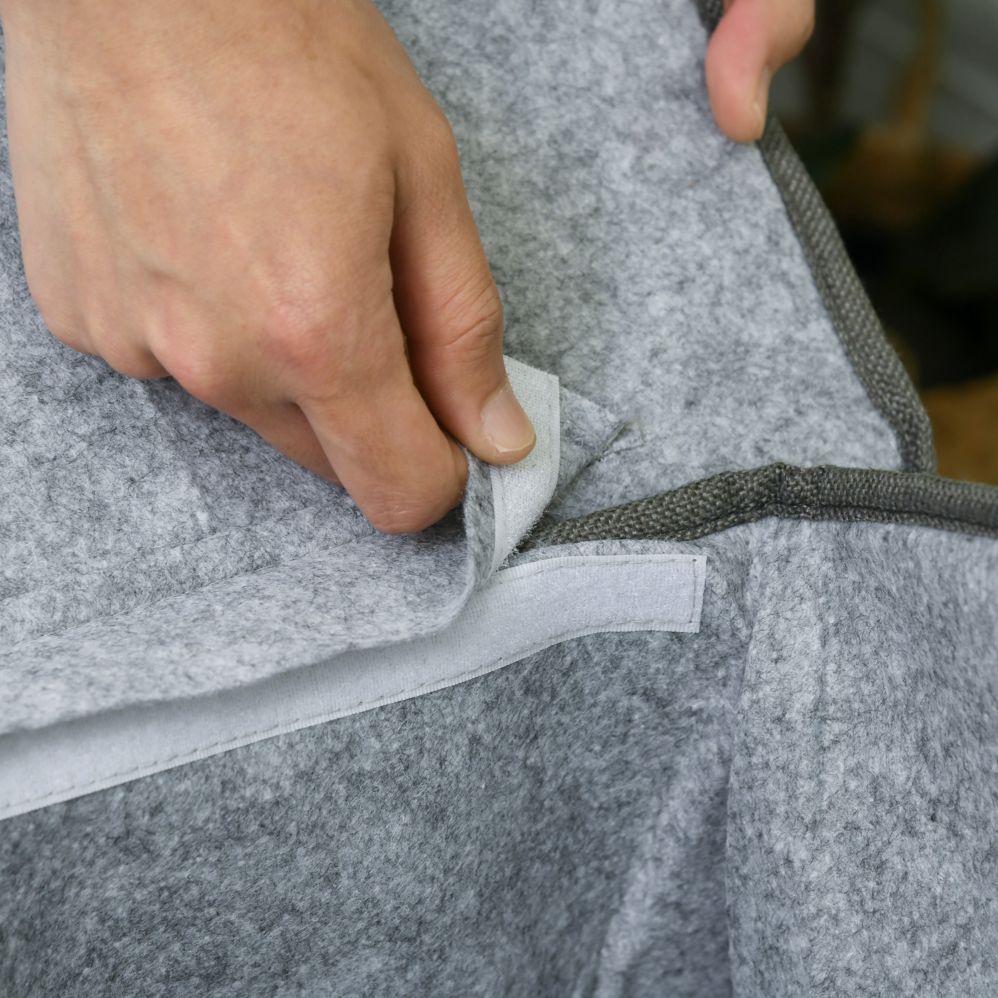 Una mano separa dos lados de tela gris con tiras de velcro blancas.
