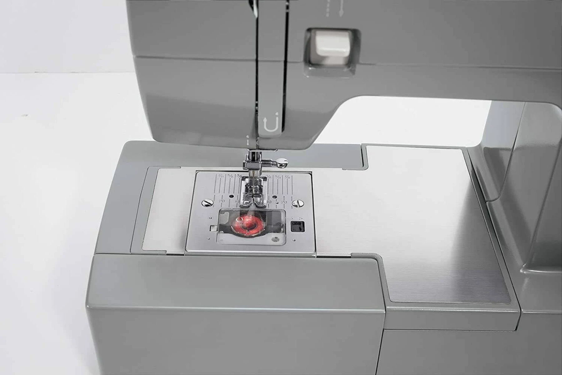 Szczegół maszyny do szycia. Szary korpus, srebrna płyta, czerwona nić, białe tło.