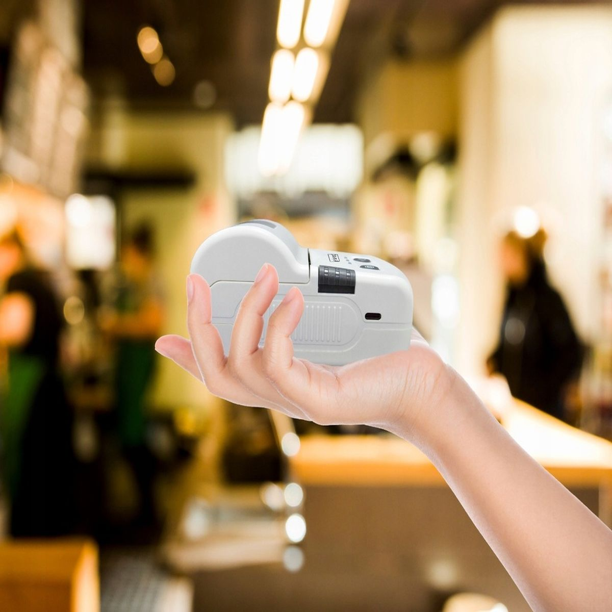 Biała drukarka trzymana w dłoni, w pomieszczeniu, z rozmytym tłem.