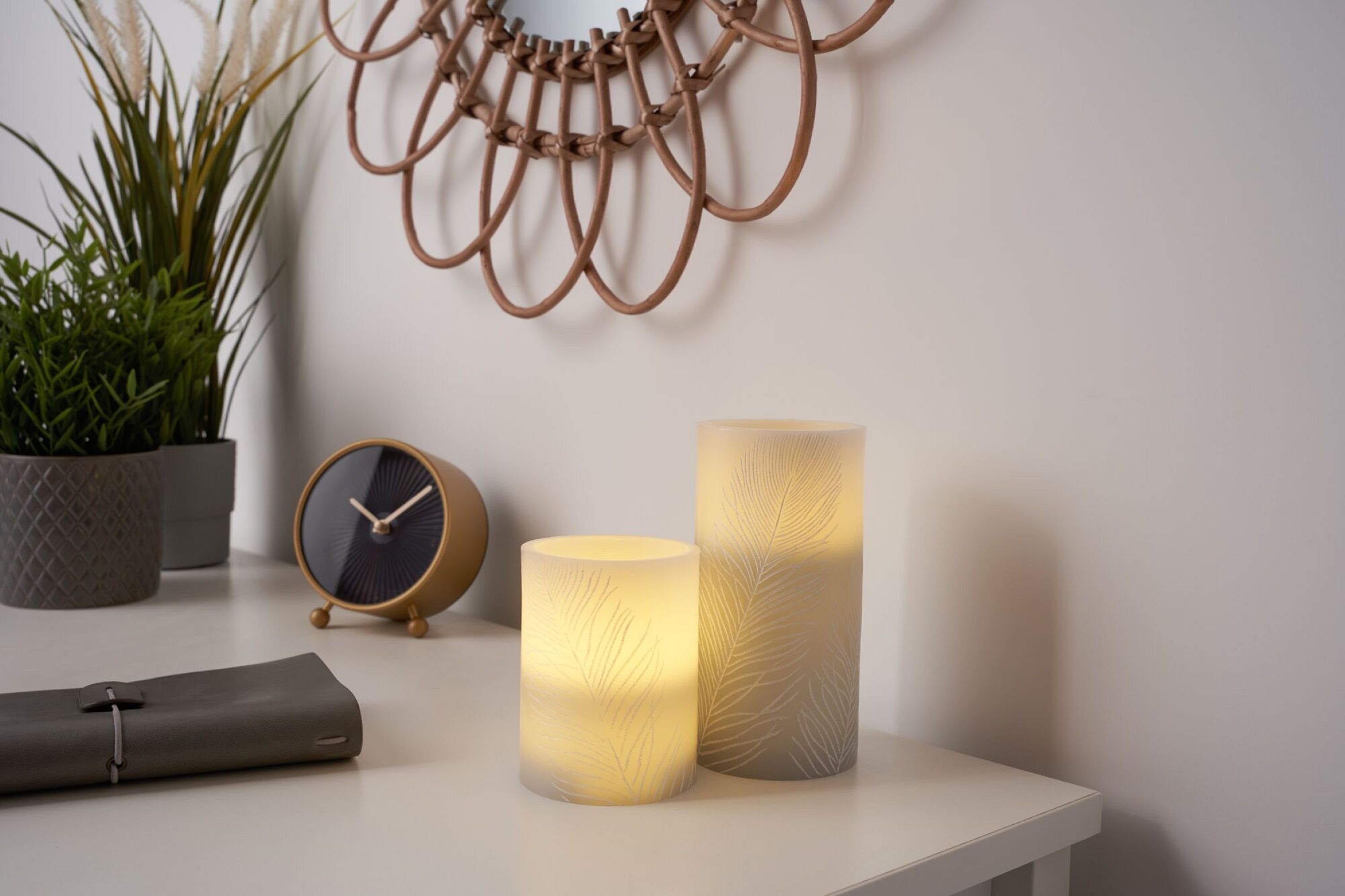 Dwie świece dekoracyjne na stole z zegarem i lustrem w tle. Świece emitują światło.