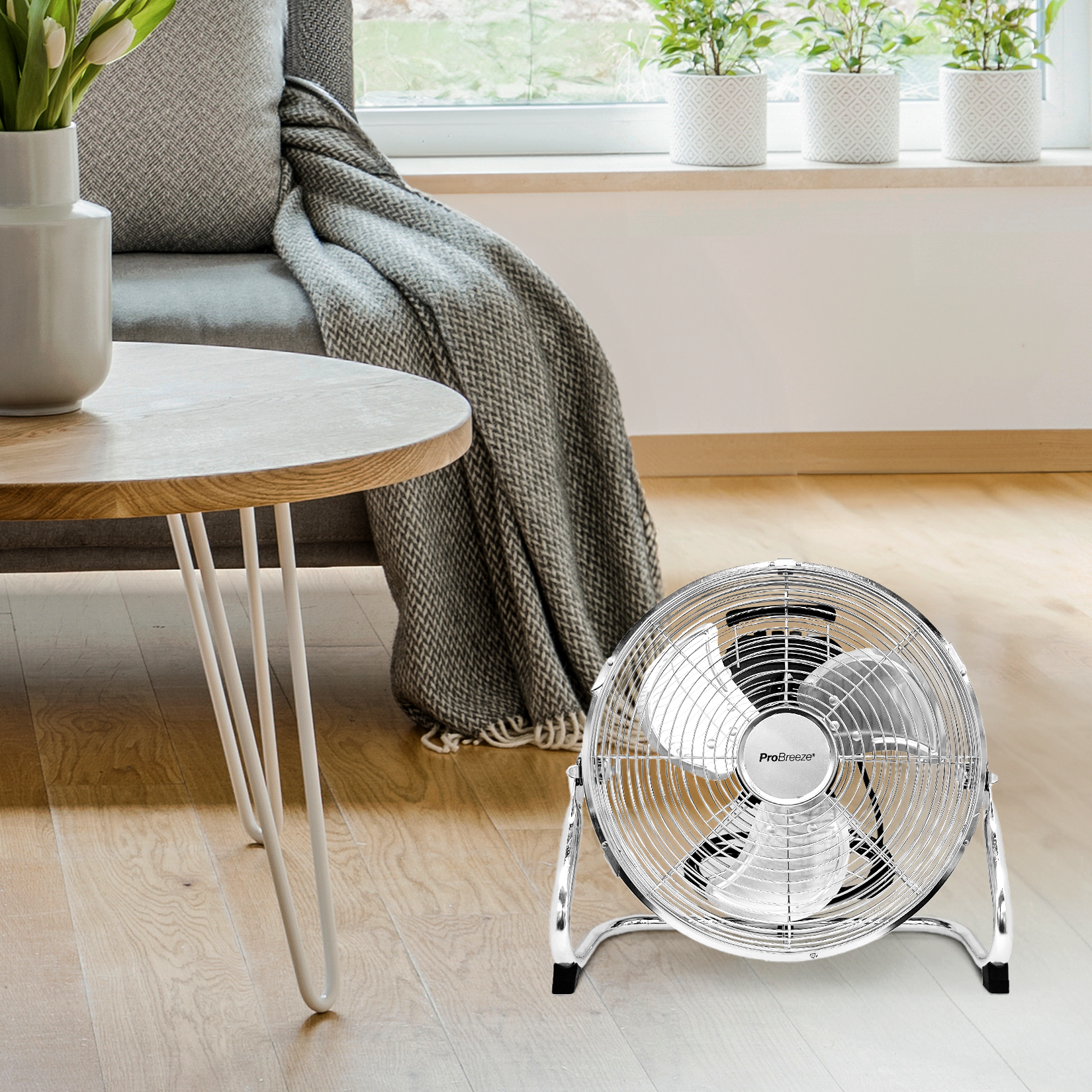 Silberner elektrischer Ventilator auf Holzboden, neben Tisch und Fenster.