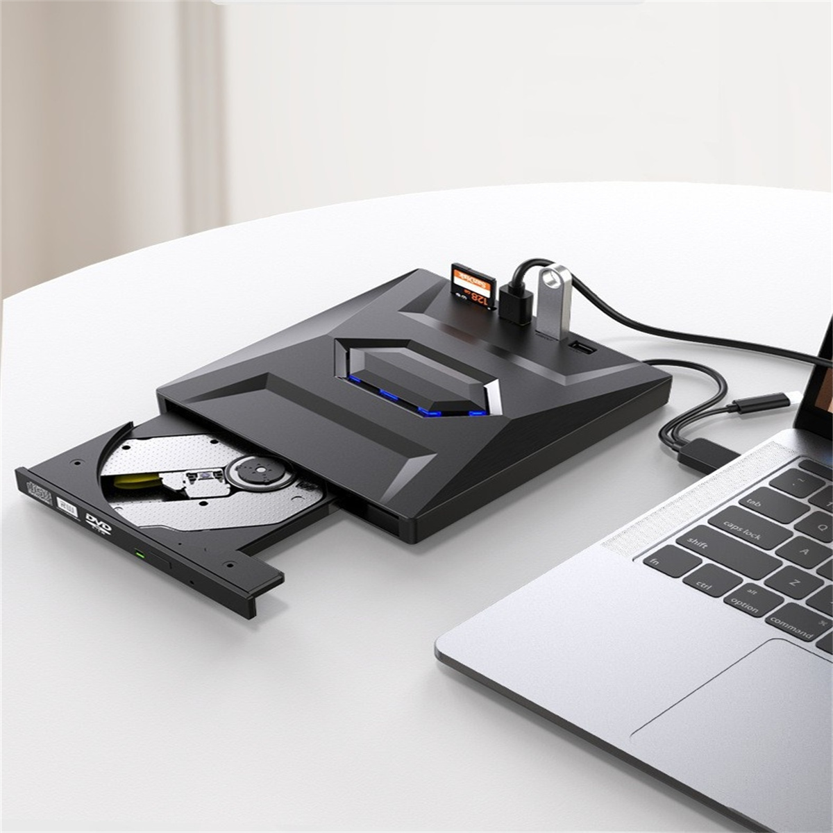 Schwarzes externes DVD-Laufwerk mit Laptop und USB-Anschlüssen auf einem weißen Tisch, mit CD im Laufwerk.