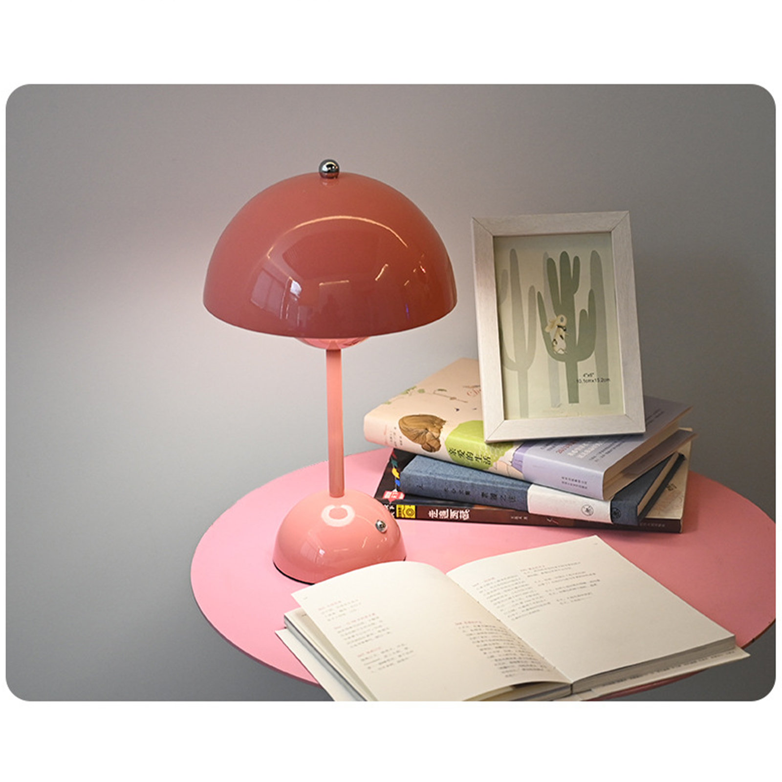 Rosa Schreibtischlampe, Bücher und ein Bilderrahmen auf einem rosa Tisch. Grauer Hintergrund.