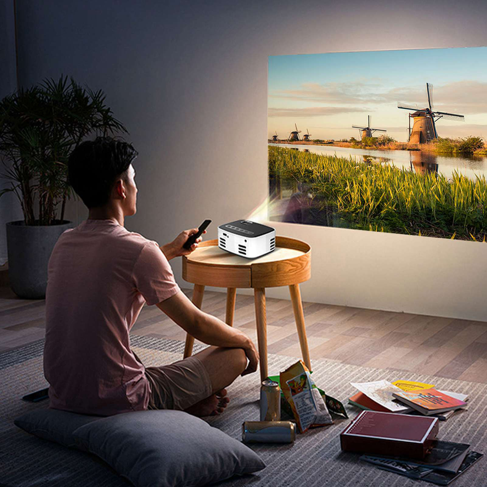 Person sitzt und betrachtet ein projiziertes Bild von Windmühlen an einer Wand. Ein Projektor steht auf einem Tisch.