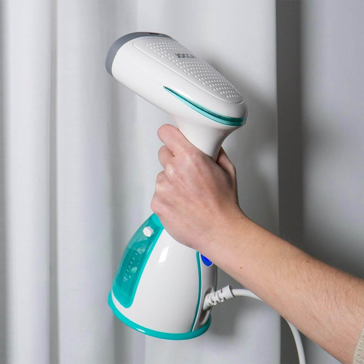 Eine Person, die Kleidung mit einem Handdampfer bedampft. Der Dampfer ist weiß und türkis.