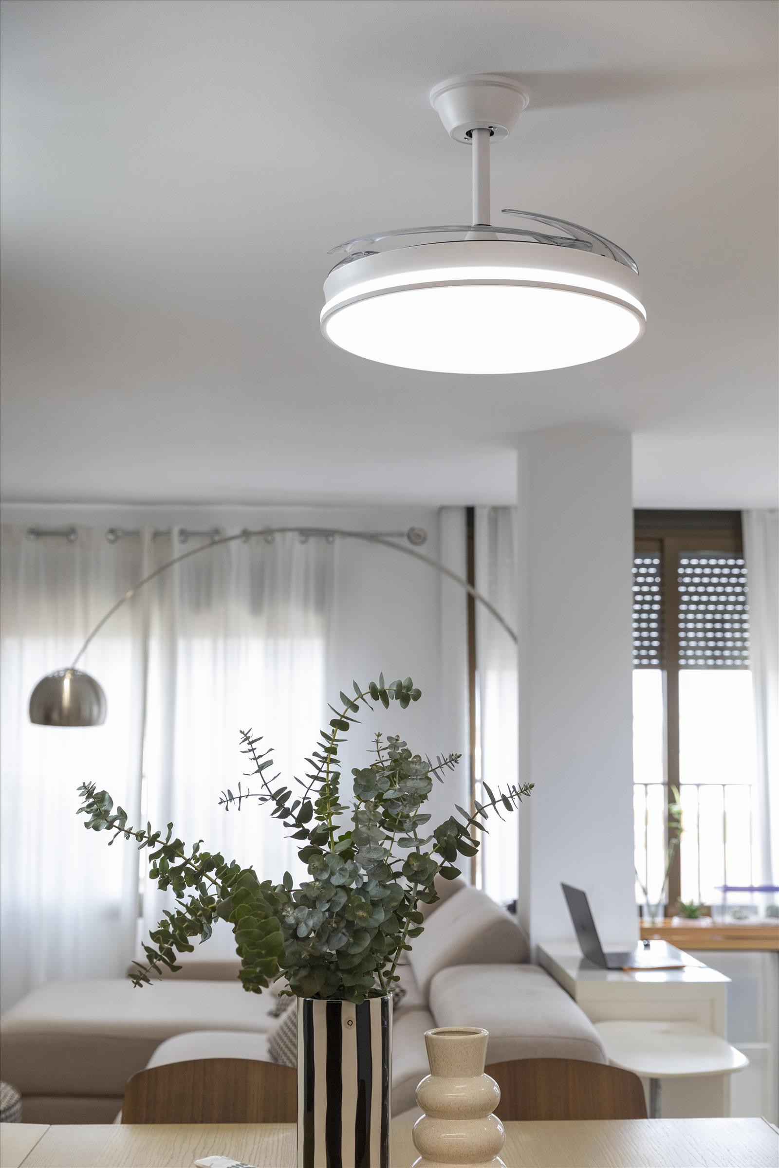 Una sala de estar moderna con ventilador de techo y planta decorativa en jarrón.
