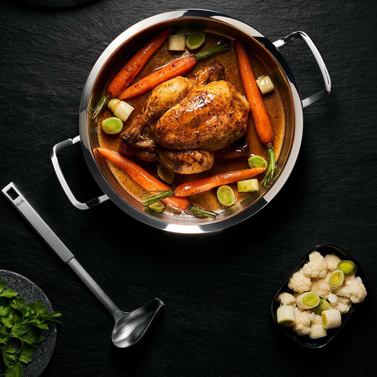 Un pollo cotto con carote e porri in una pentola, e un po' di cavolfiore.