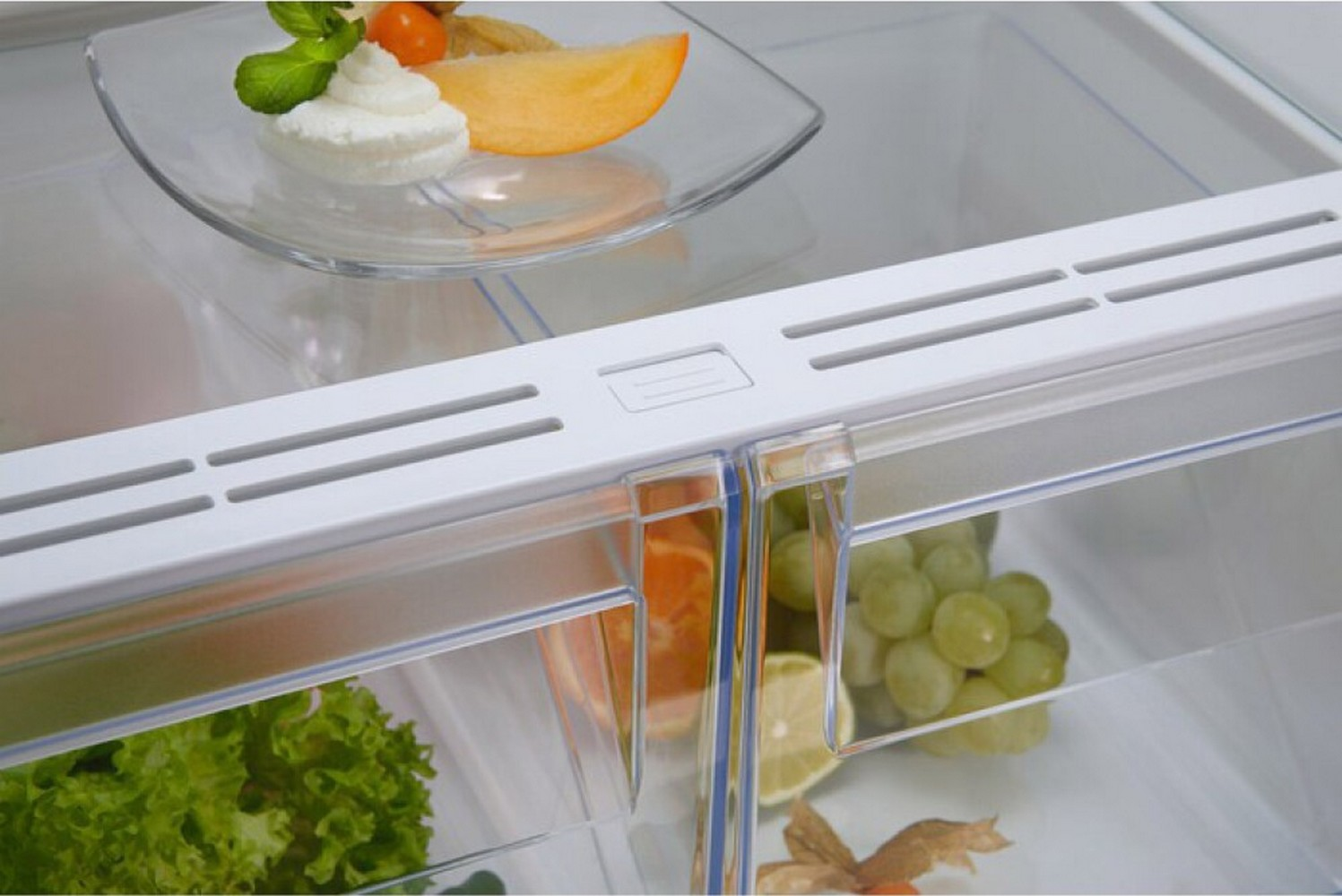 All'interno di un frigorifero, un piatto con panna montata e frutta si trova sopra due cassetti trasparenti per prodotti.