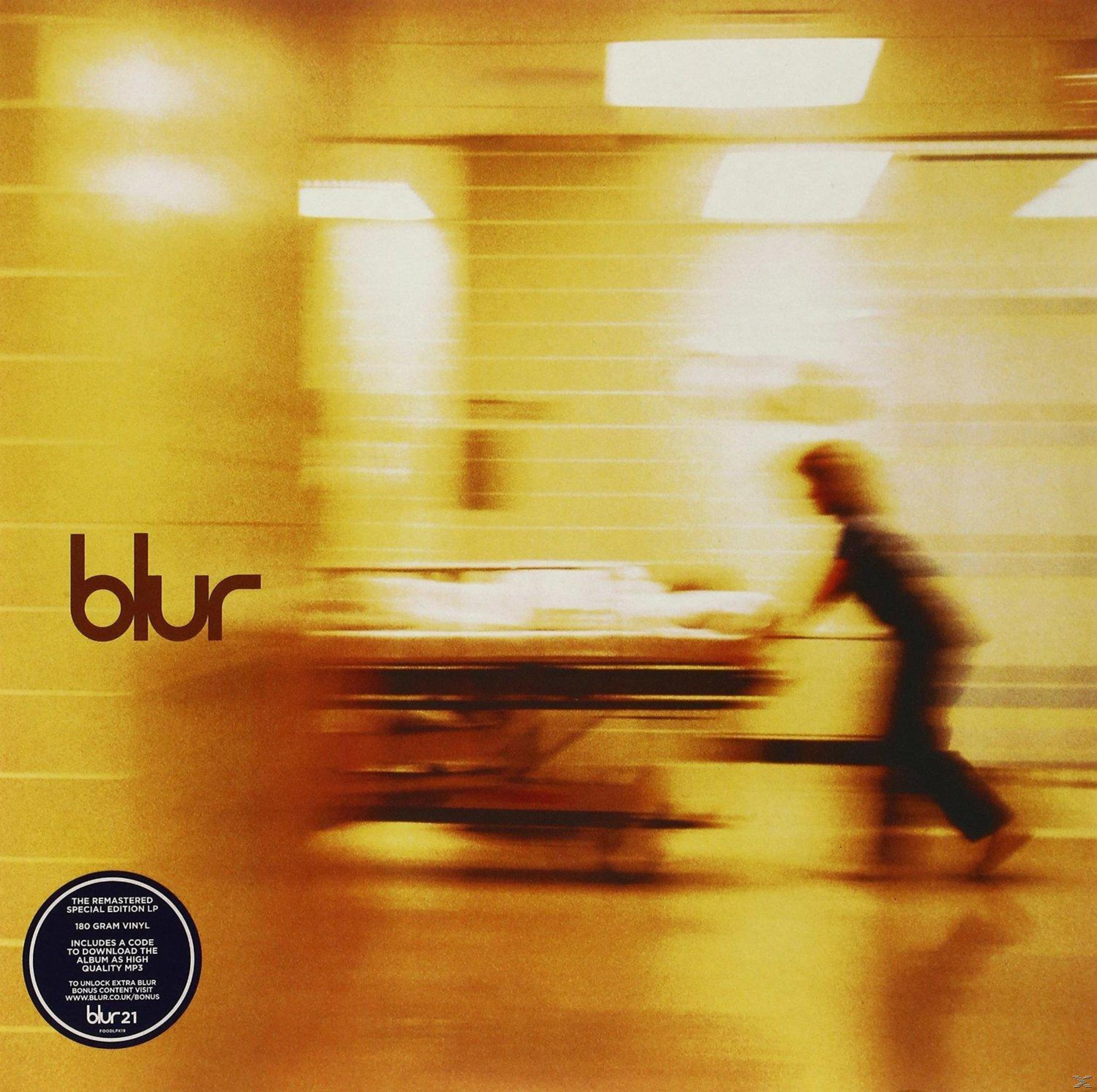 Copertina dell'album Blur. Figura sfocata che spinge una barella in un corridoio illuminato di giallo. Il nome della band è in alto a sinistra.