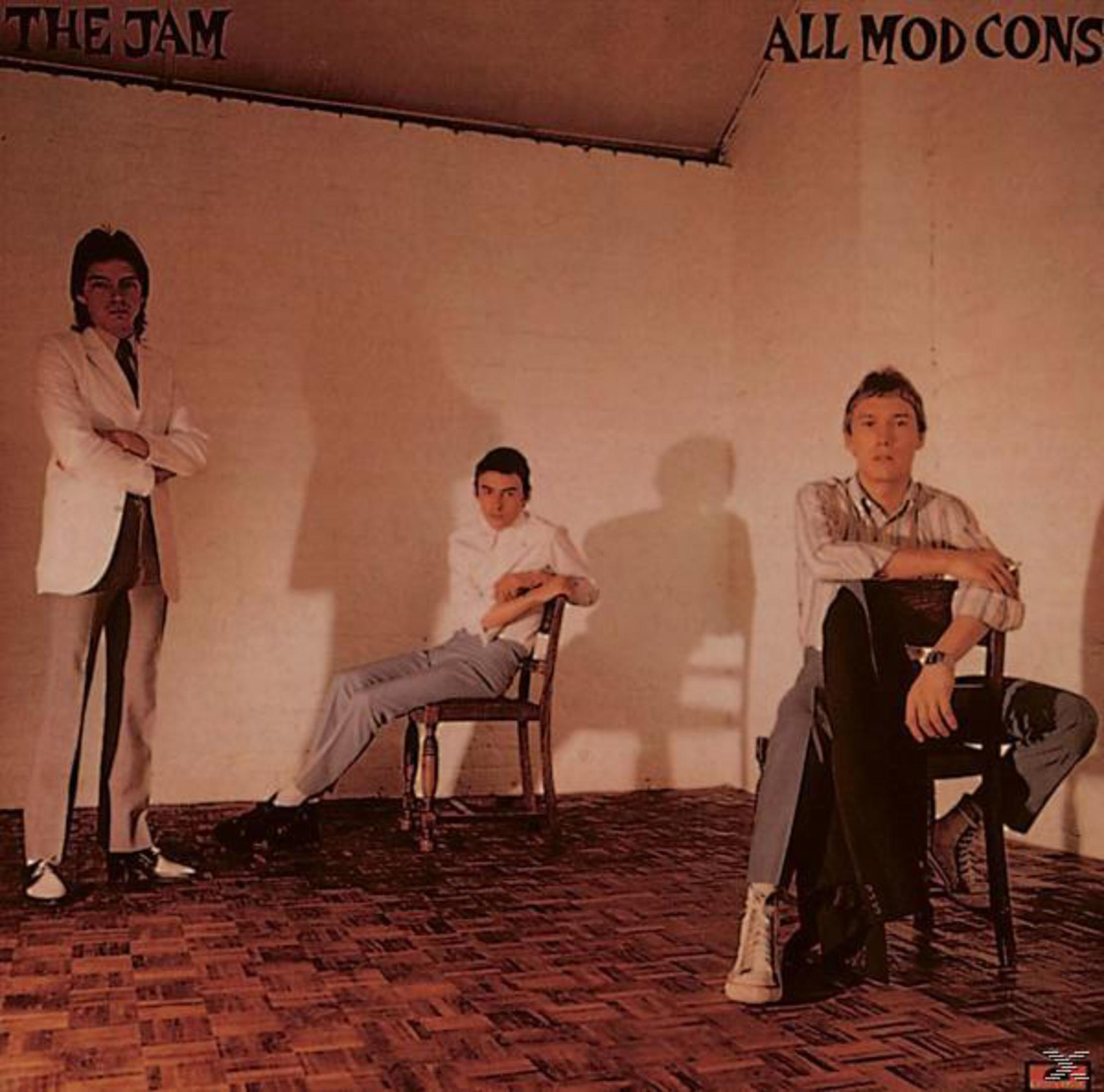 The Jam albumhoes: Drie mannen in een kamer, twee zitten, een staat. Neutrale muur, patroonvloer.