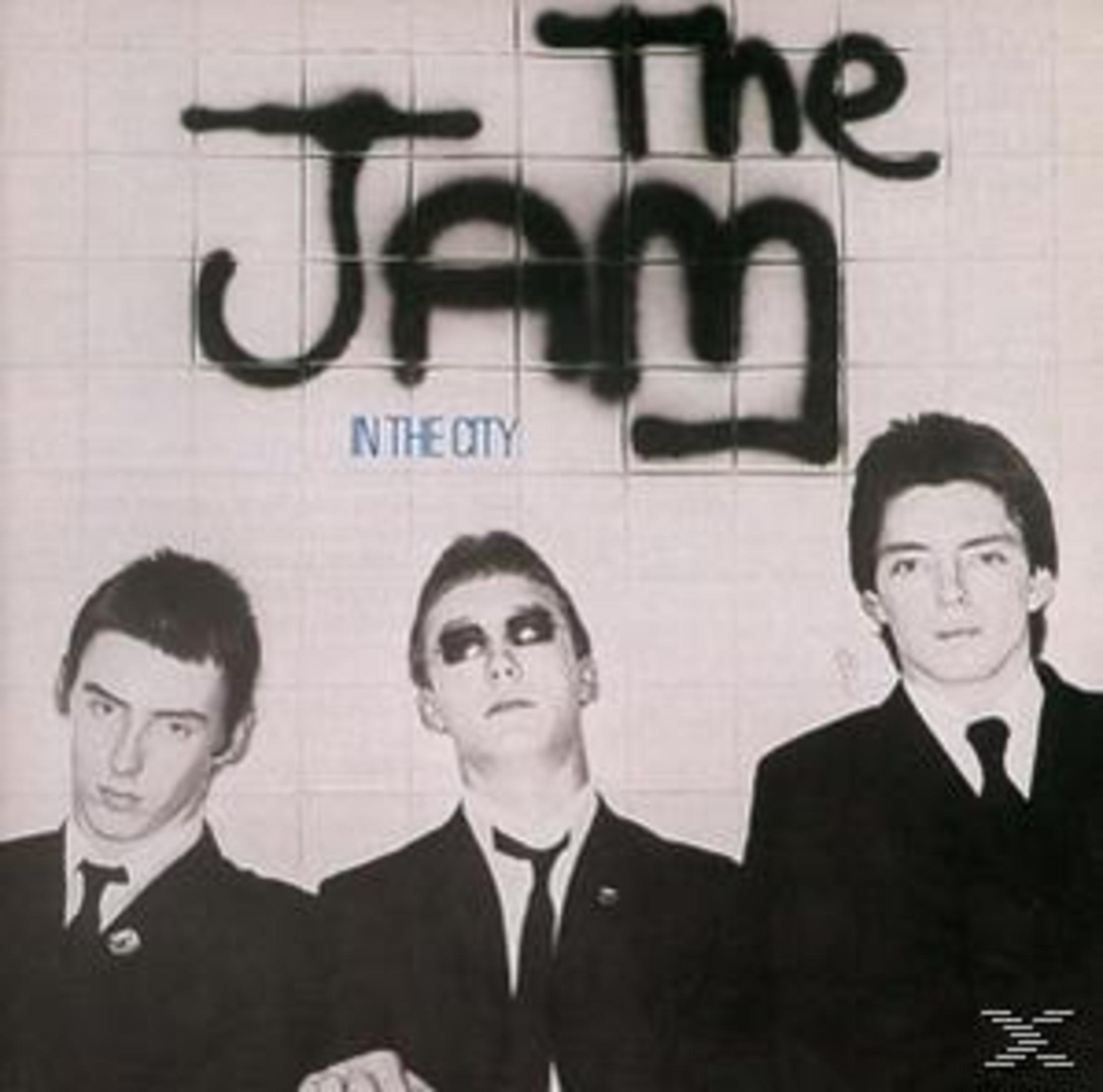 Copertina dell'album: The Jam, tre uomini in giacca e cravatta. Testo: The Jam, In the City. Sfondo piastrellato bianco.