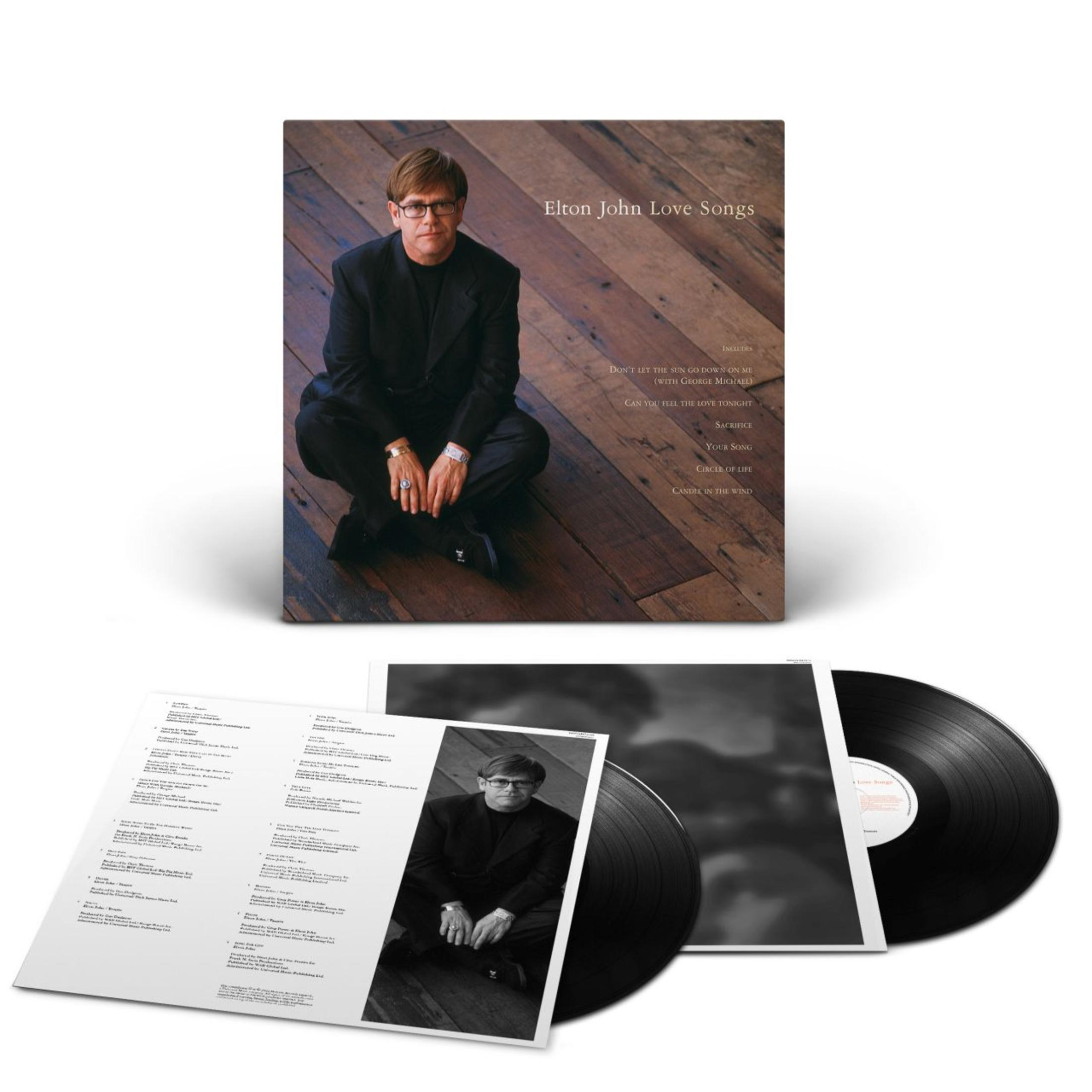 Elton John, in een zwart pak, zit op een houten vloer, een vinylplaat en een albumhoes.