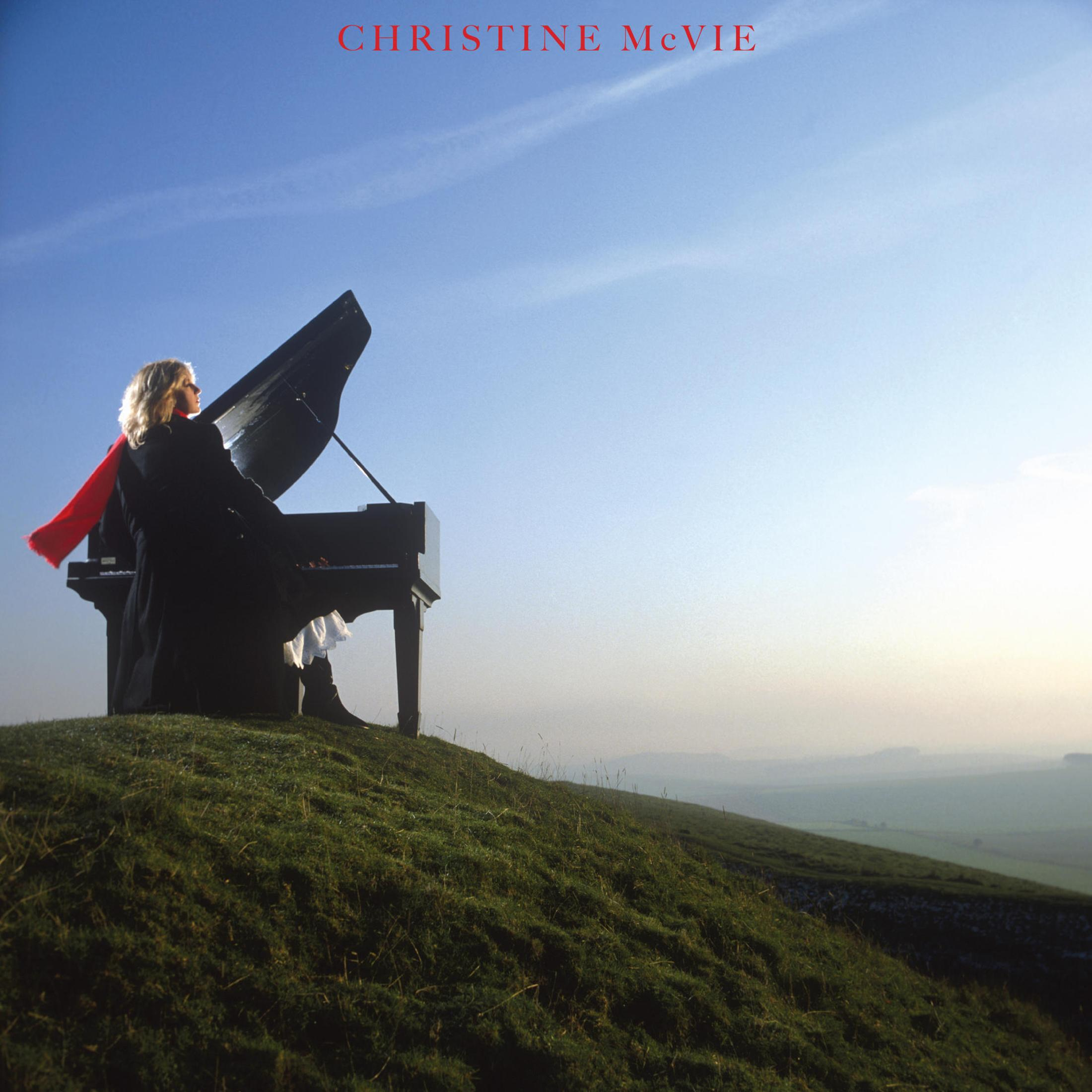Christine McVie toca el piano en una colina. Bufanda roja, cielo azul y un piano.
