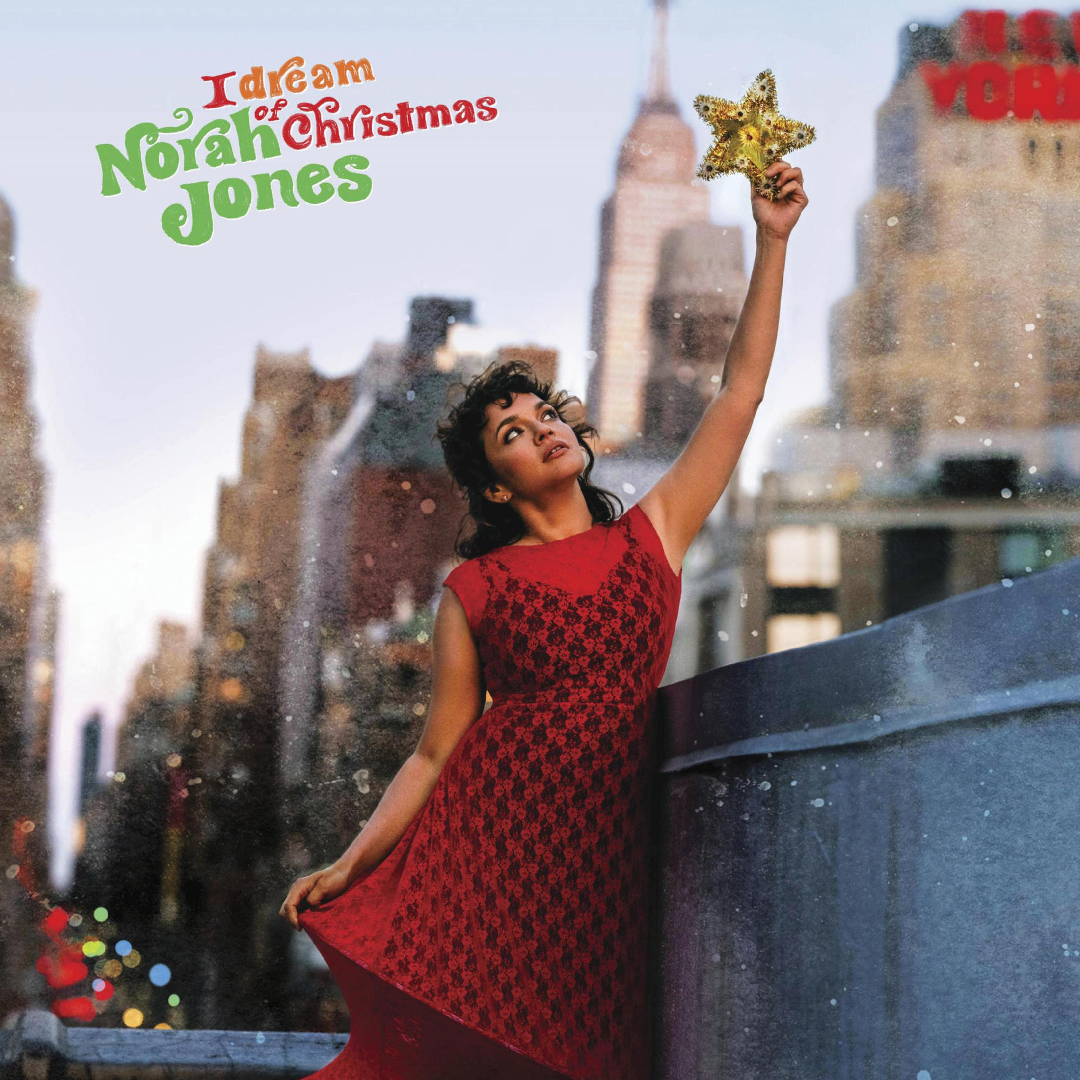 Copertina dell'album di Norah Jones. Tiene una stella sopra una città. Abito rosso, neve che cade, titolo in alto.
