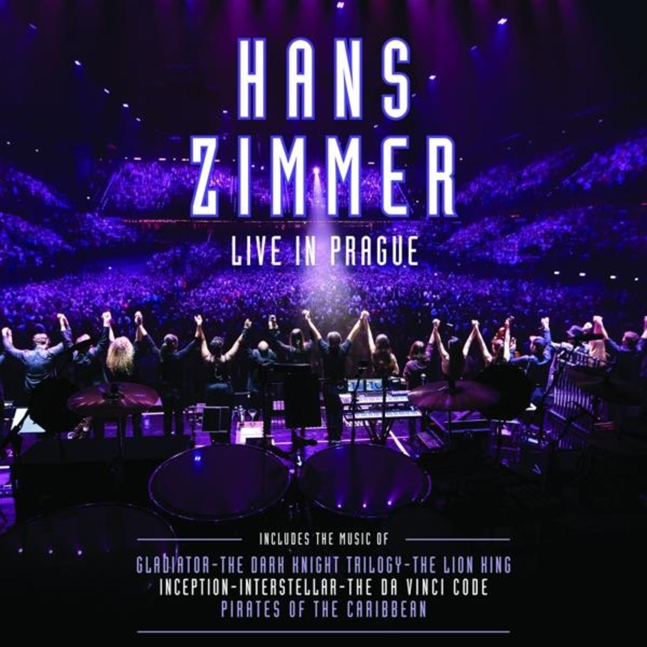Un palco con una band e un pubblico. Il testo "Hans Zimmer Live in Praga" è sopra il palco.