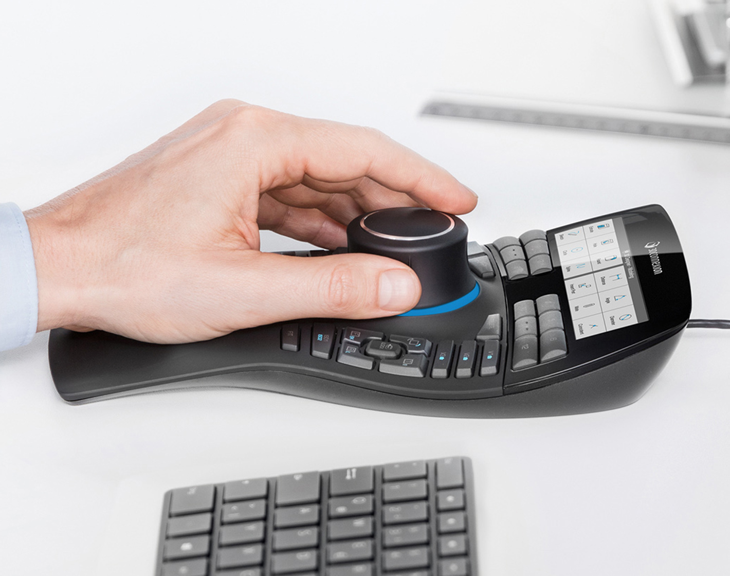 A person's hand using a 3Dconnexion CAD mouse, with a keyboard in the foreground.