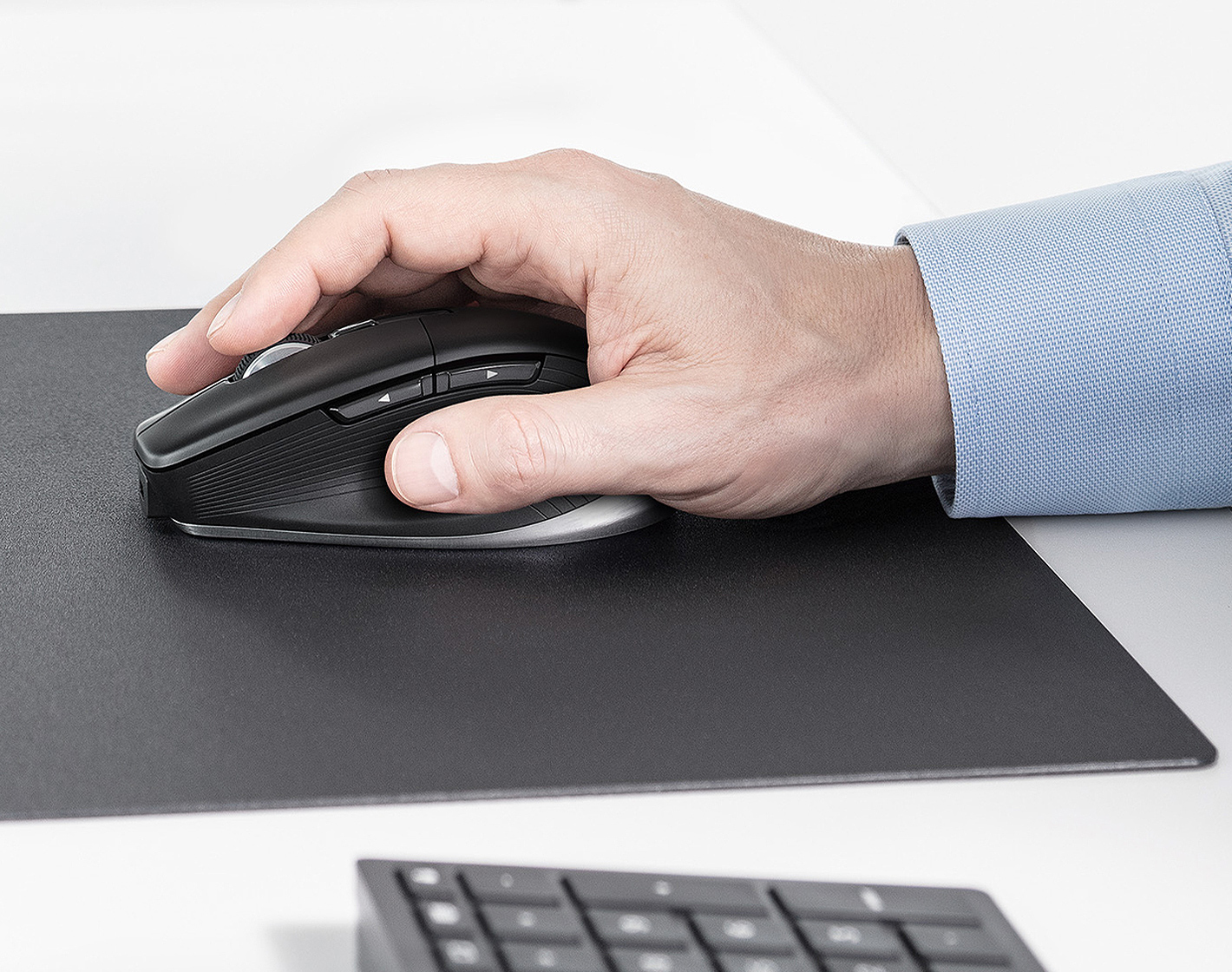 A hand is using a black mouse on a black mousepad. A keyboard is at the bottom.